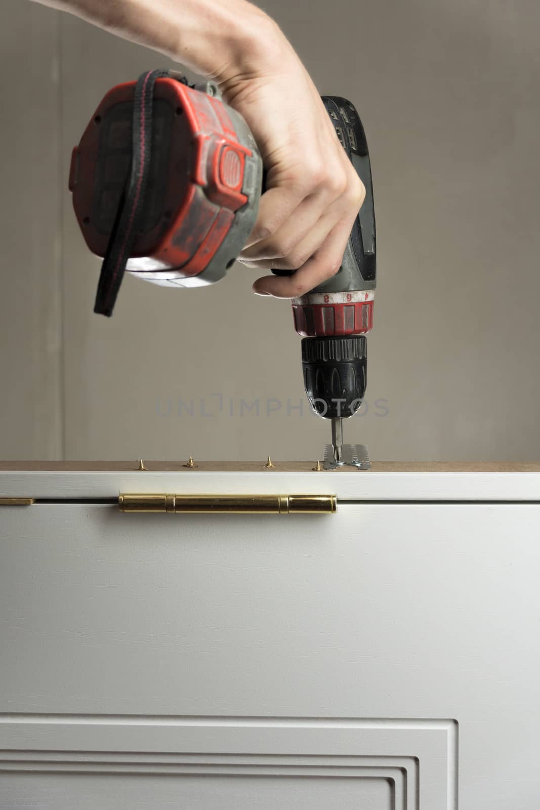 A worker twists a screw into the Board with a drill. The handyman does housework and improves the dwelling. Photographed vertically