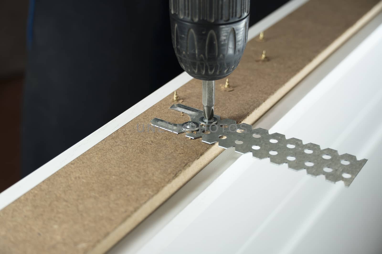 A worker twists a screw into the Board with a drill. The handyma by YevgeniySam