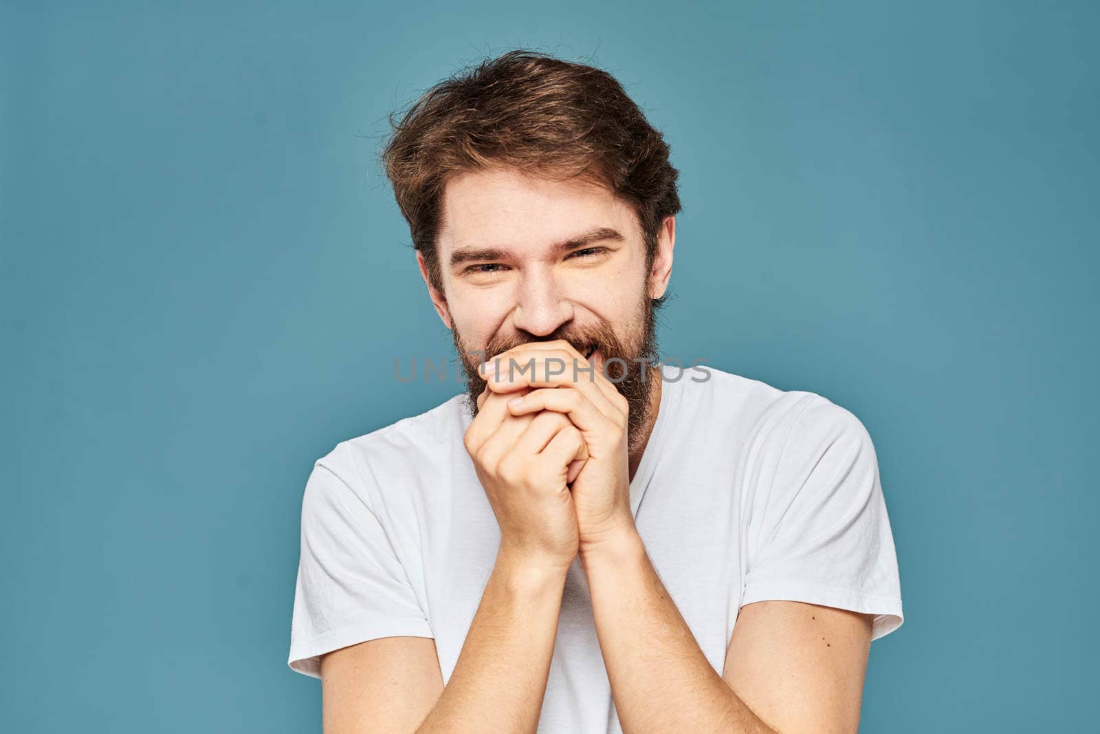 A bearded man in a white T-shirt gestures with his hands emotions blue background. High quality photo