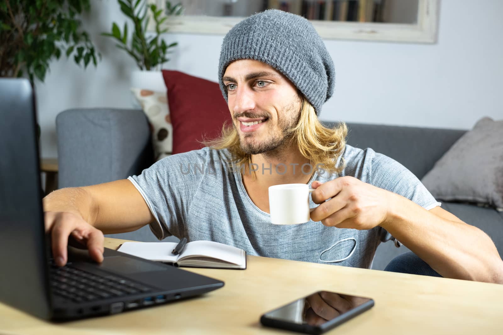 Handsome young caucasian man using computer working at home and talking with mobile feeling happy with smile showing teeth
