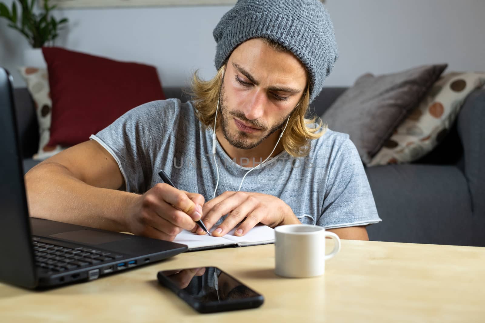Handsome young caucasian man using computer working at home and learning online and writing notes