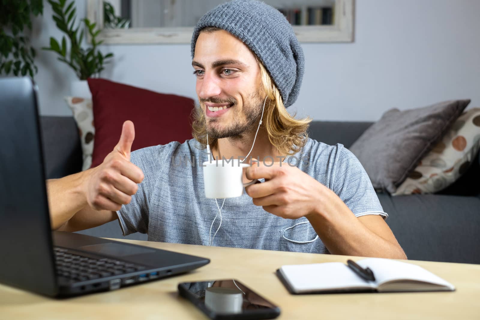 Handsome young caucasian man using computer working at home and talking with mobile feeling happy with smile showing teeth with thumbs up