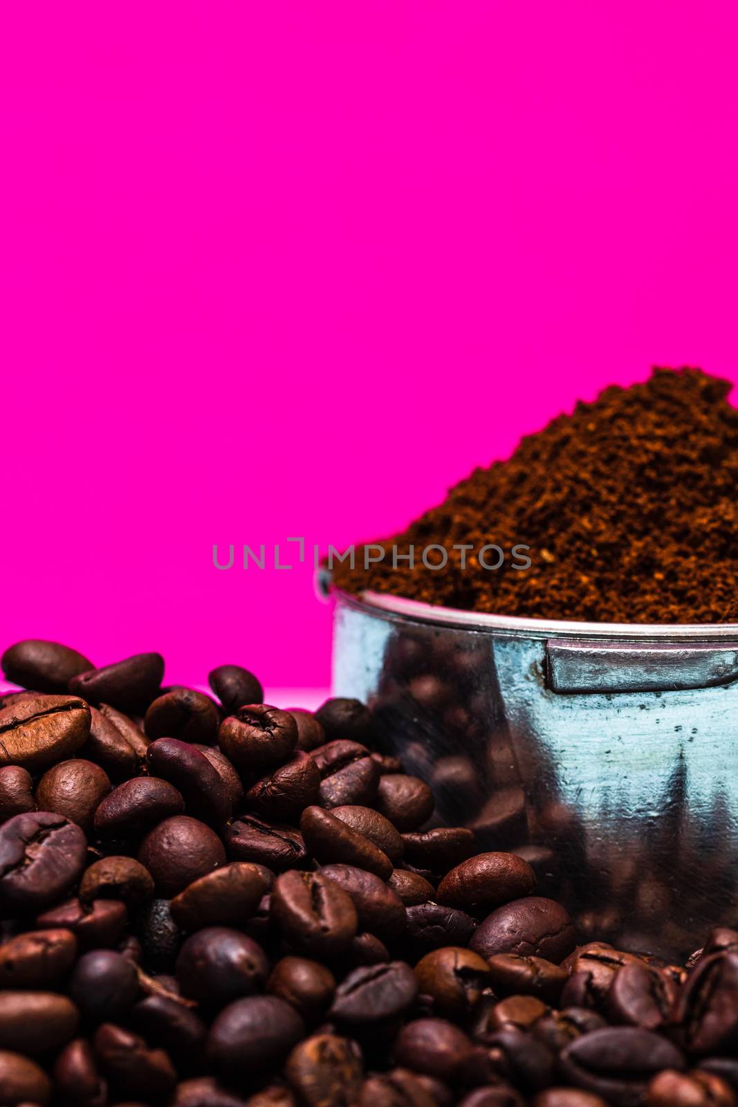 Coffee beans and portafilter with ground coffee in a composition on a pink background.