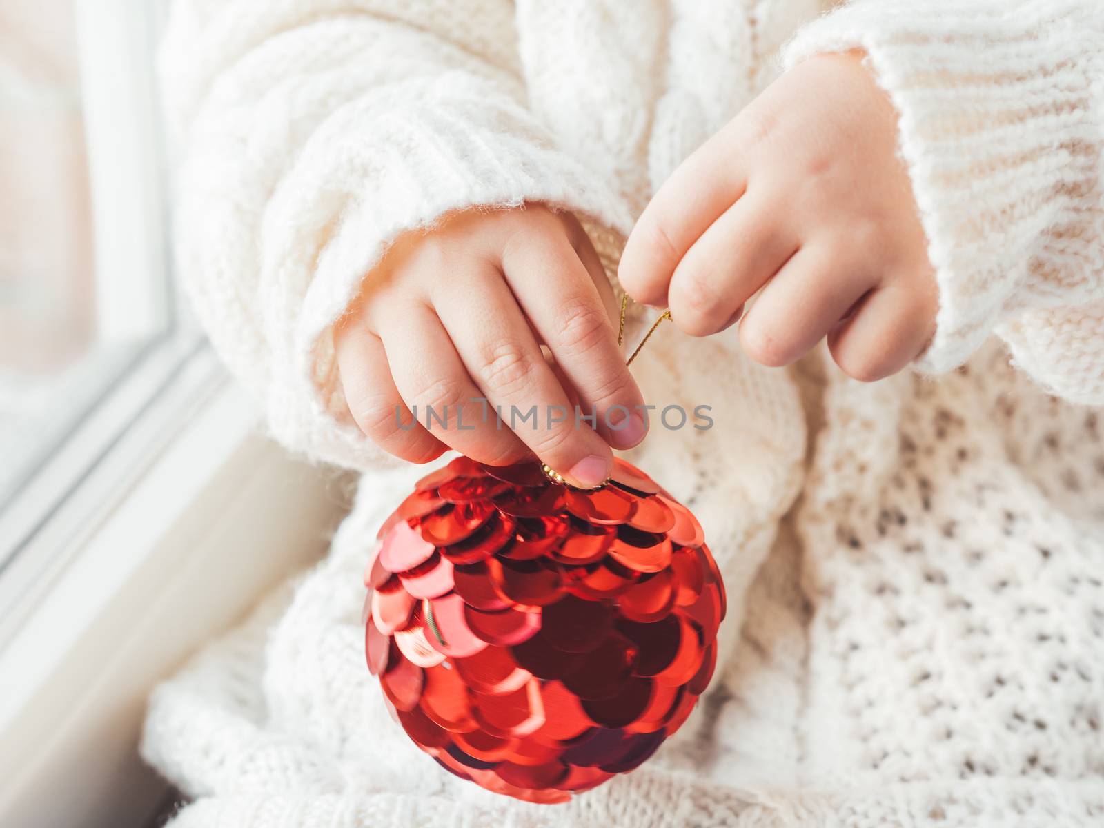 Kid with red decorative ball for Christmas tree. Boy in cable-knit oversized sweater. Cozy outfit for snuggle weather. Winter holiday spirit. New year.