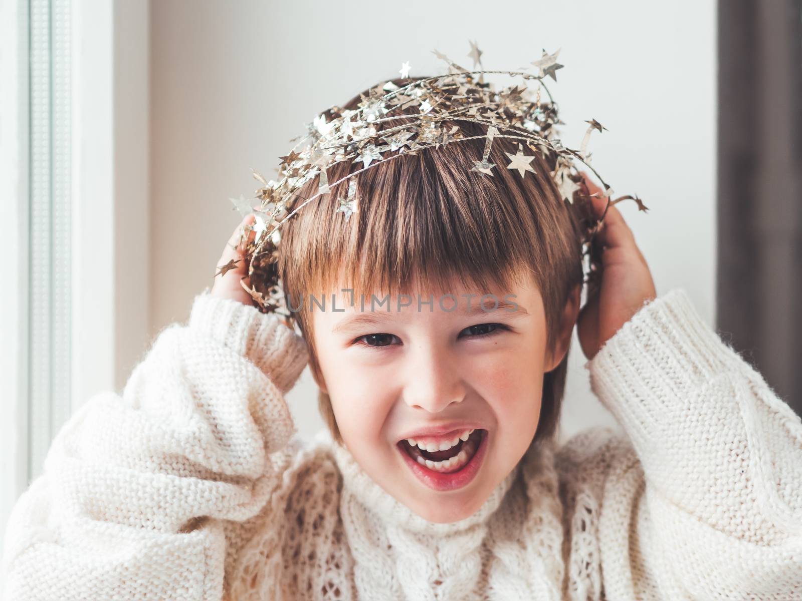 Kid with decorative star tinsel for Christmas tree. Boy in cable-knit oversized sweater. Cozy outfit for snuggle weather. Winter holiday spirit.New year.