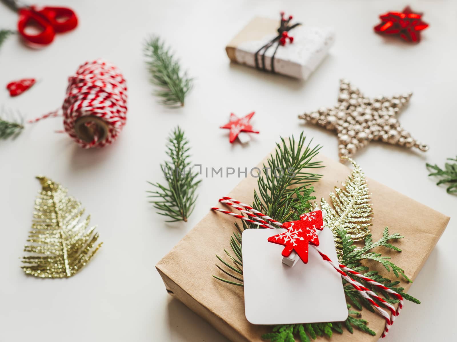 Christmas DIY presents wrapped in craft paper with fir tree branches. Red decorations in shape of Christmas tree. New Year gifts. Festive background. Winter holiday spirit.