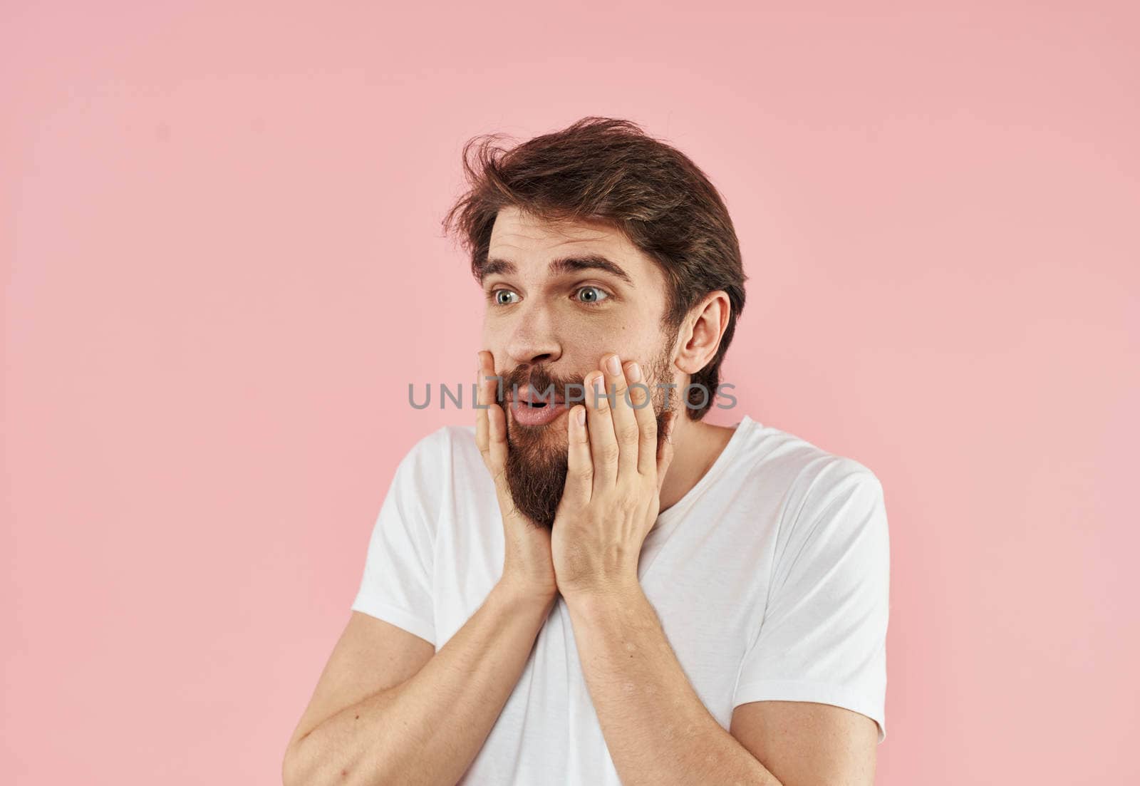 Emotional man holds his hand near his face on a pink background Copy Space. High quality photo