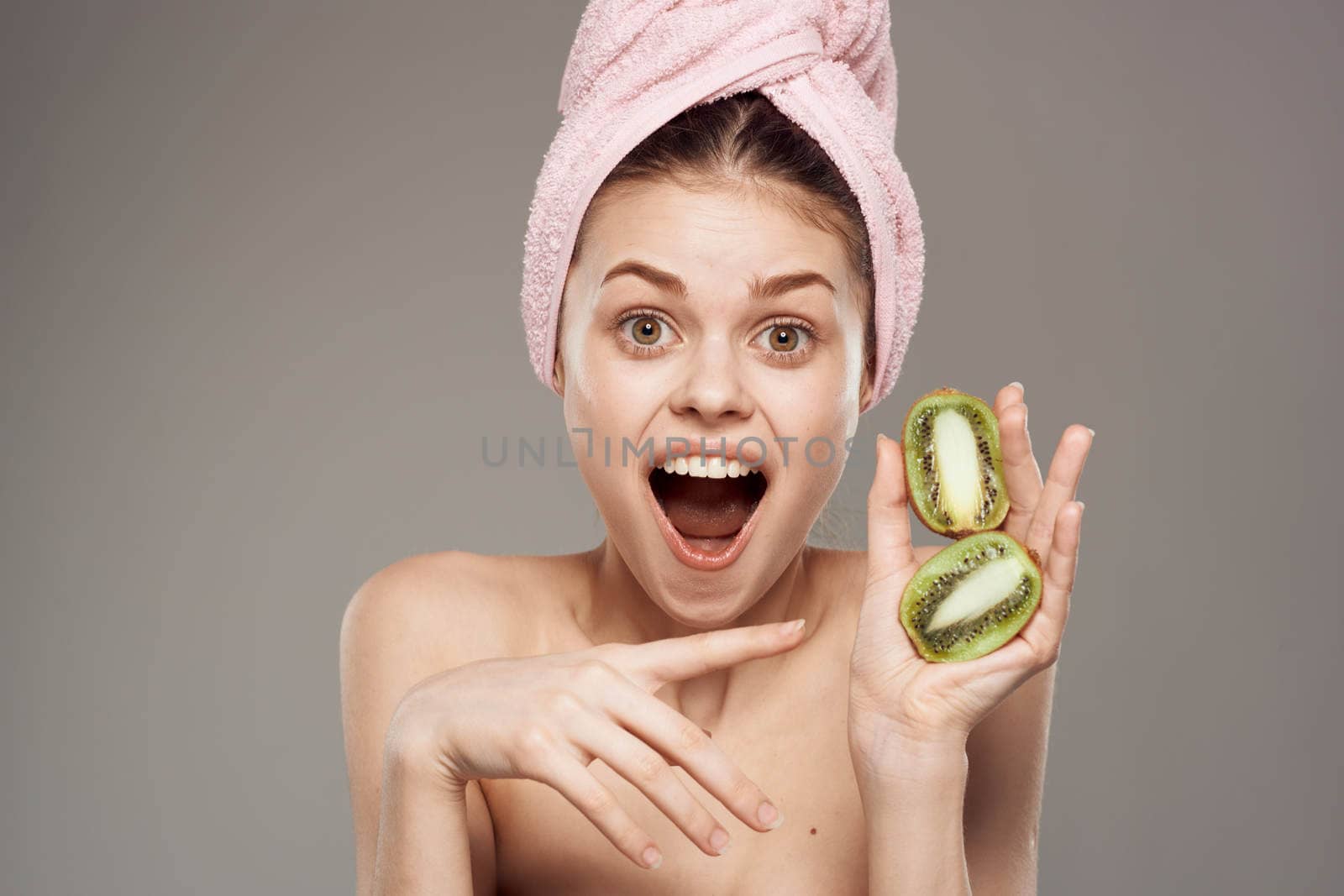 cheerful woman with a pink towel on her head surprised look Kiwi hand vitamins gray background. High quality photo