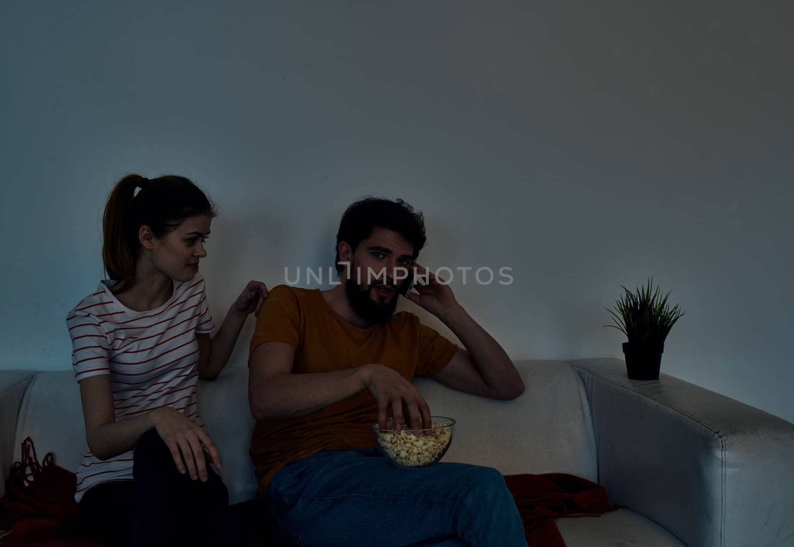 emotional woman and man with a plate of popcorn watching tv in the evening indoors by SHOTPRIME