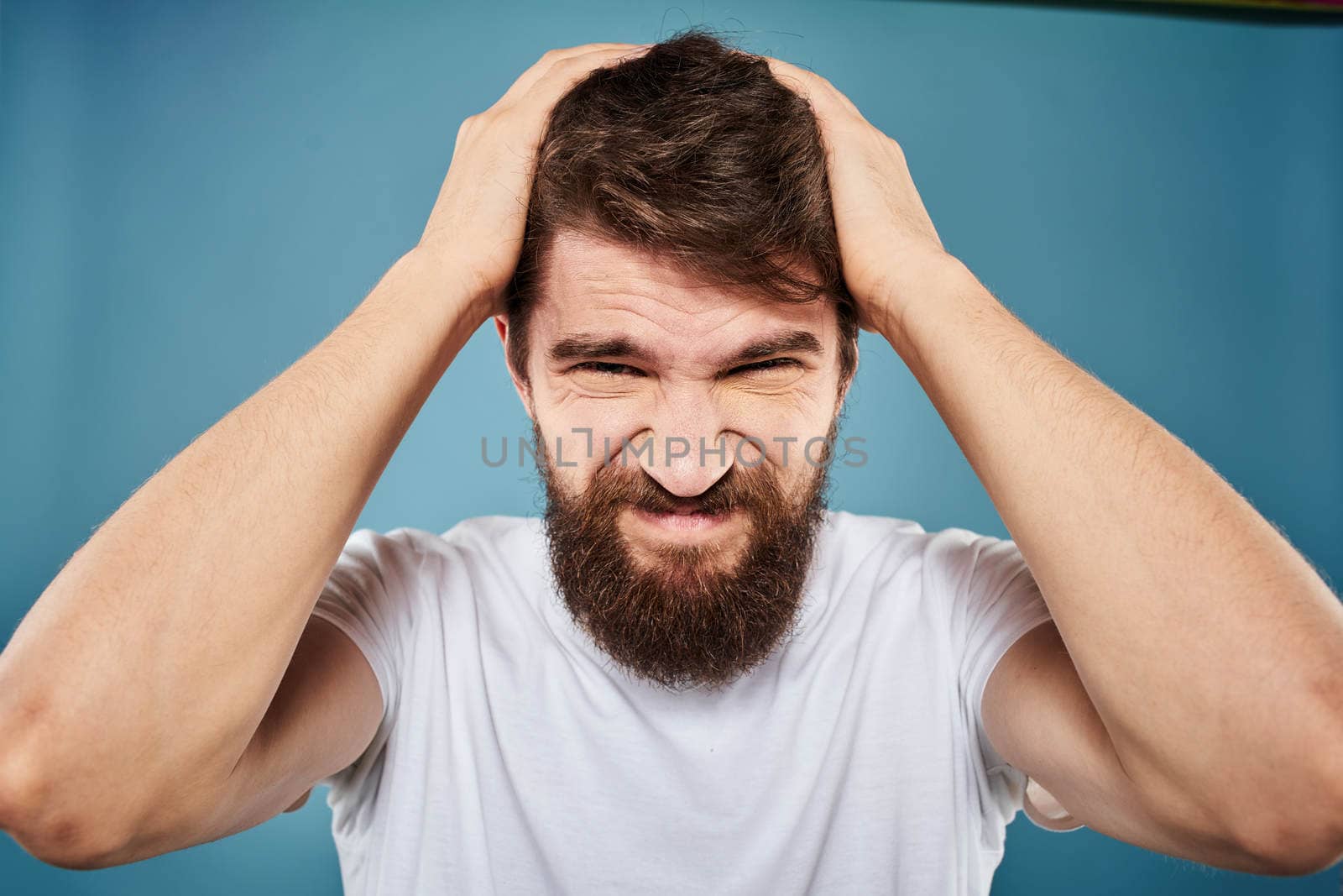 Bearded man displeased facial expression emotions close-up blue background white t-shirt. High quality photo