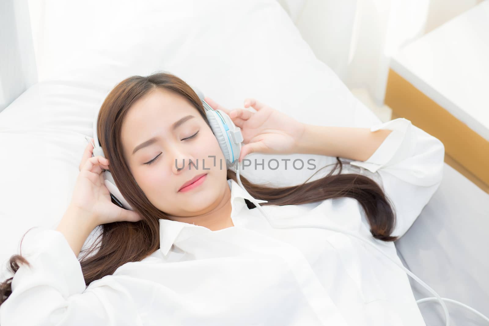 Beautiful asian young woman enjoy listen music with headphone while lying in bedroom, relax girl with earphone internet online, leisure and technology concept.