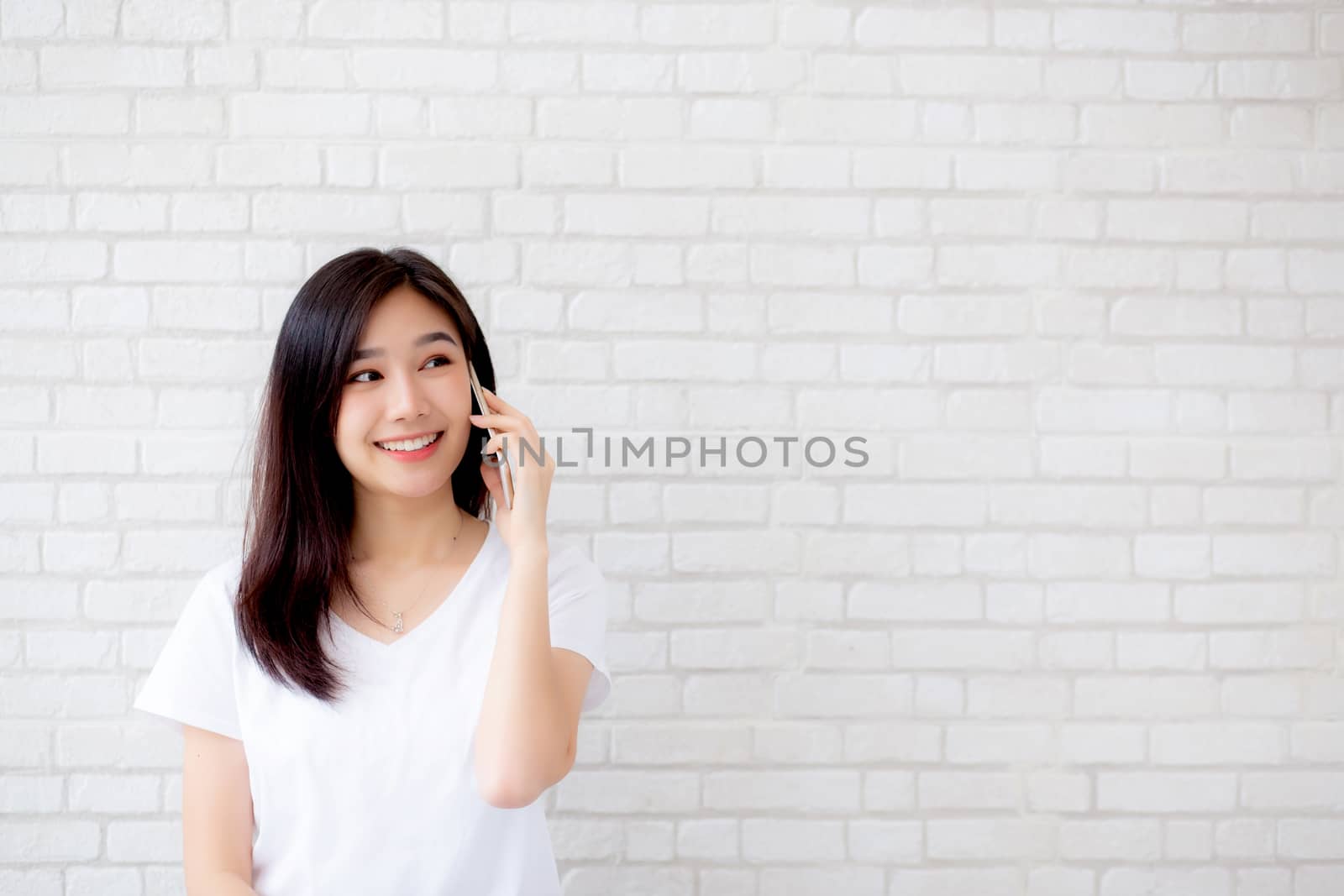 Beautiful of portrait young asian woman talk smart phone and smile standing on cement brick background, freelance female calling telephone, communication of mobile concept.