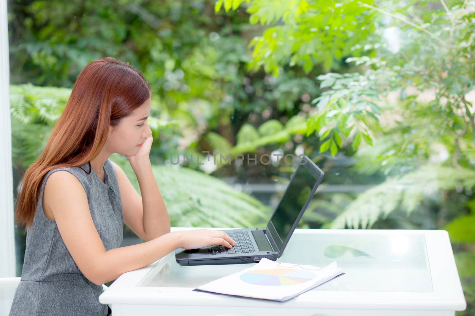 Beautiful of portrait asian young woman working online on laptop computer with graph paper sitting at office, professional female freelancer using notebook with connect to internet for distance job, business concept.