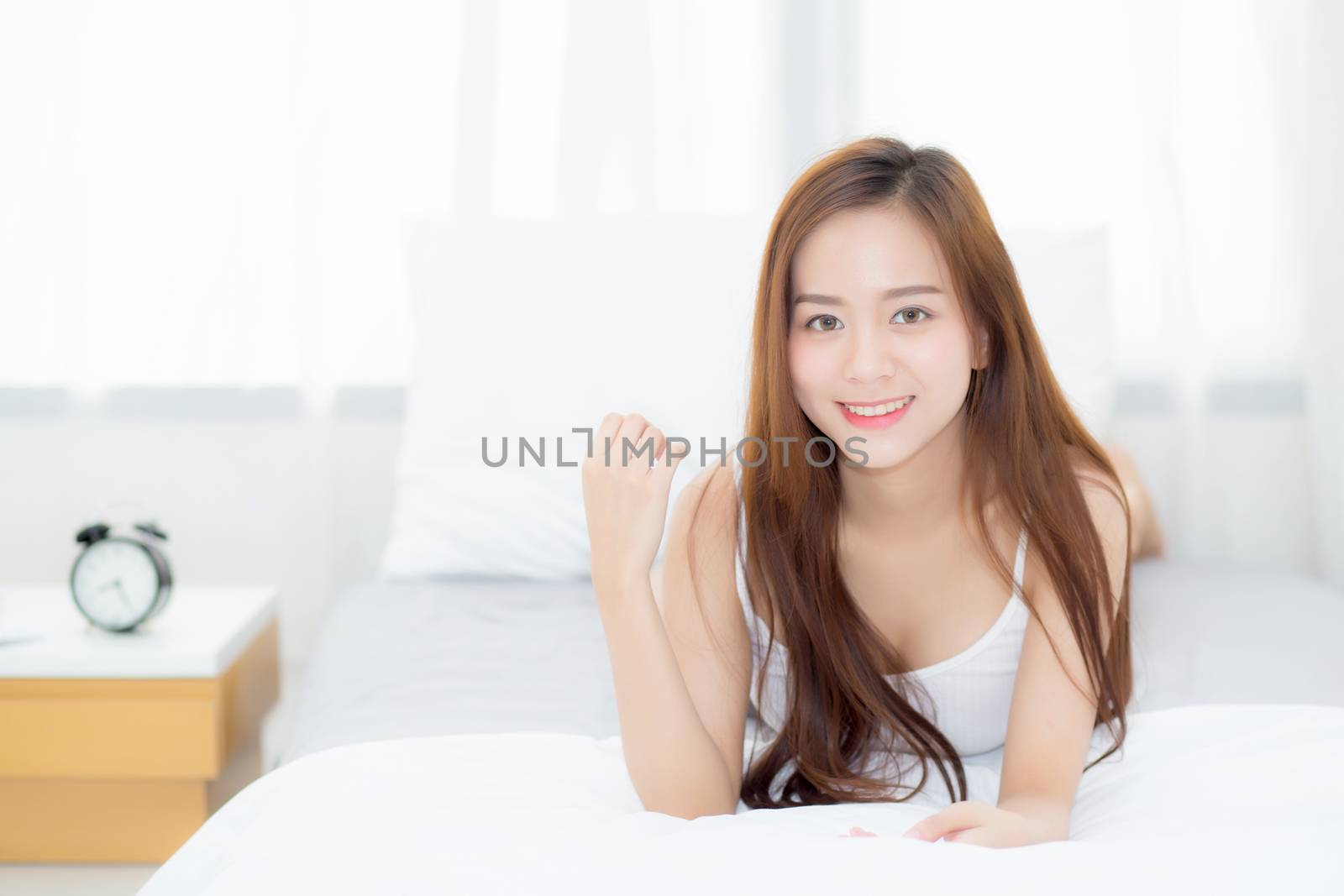 Beautiful portrait young asian woman lying and smile while wake up with sunrise at morning, lifestyle and relax concept.