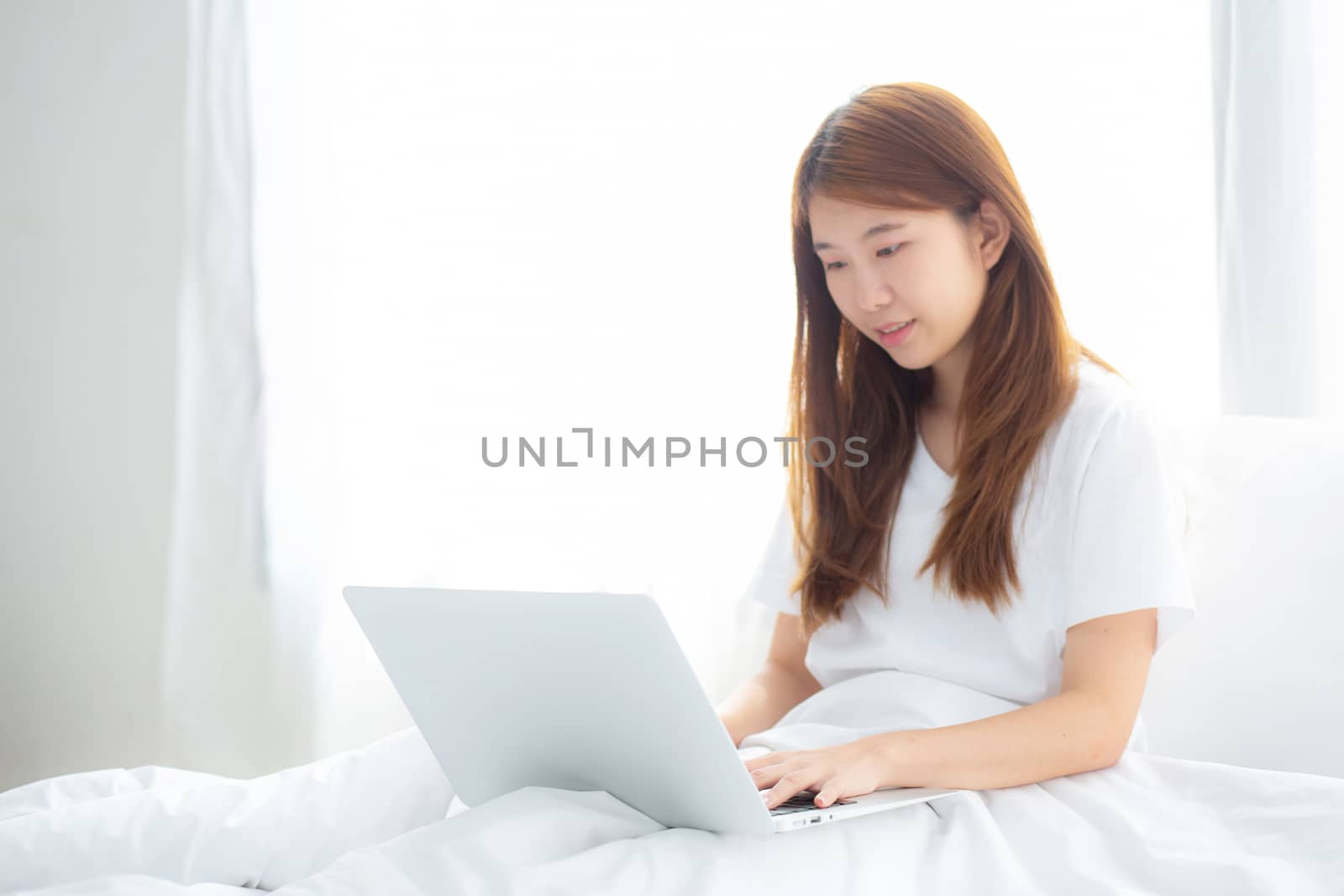 Portrait of beautiful asian young woman setting on bed using lap by nnudoo