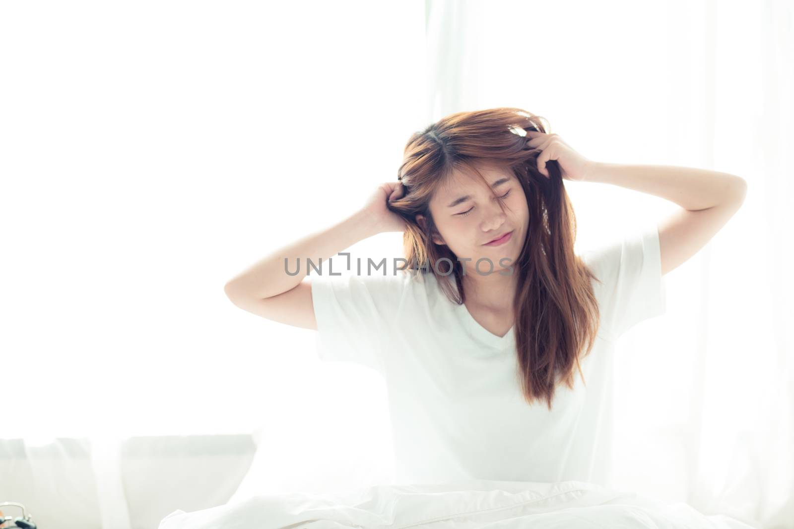 Beautiful young asian woman stretch and relax in bed after wake up morning at bedroom, back view, new day and resting for wellness, lifestyle concept.