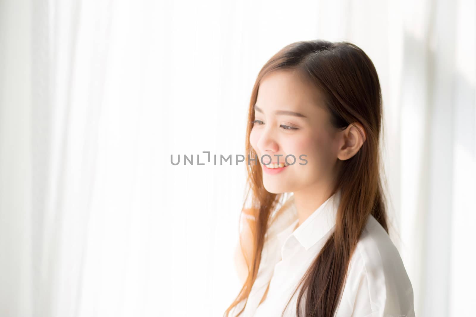 Portrait of beautiful young asian woman standing the window and smile while wake up with sunrise at morning, lifestyle and relax concept.