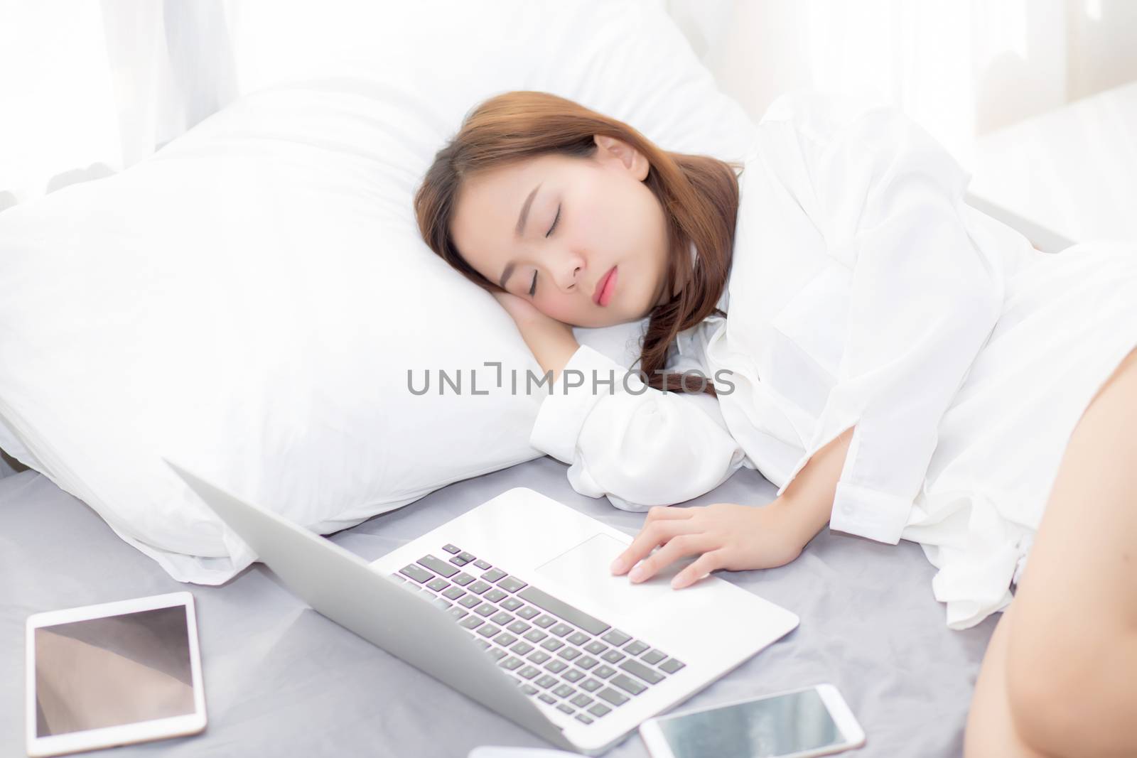Beautiful young asian woman with laptop lying down in bedroom, girl tired sleep with computer notebook and tablet, resting and healthcare concept. 