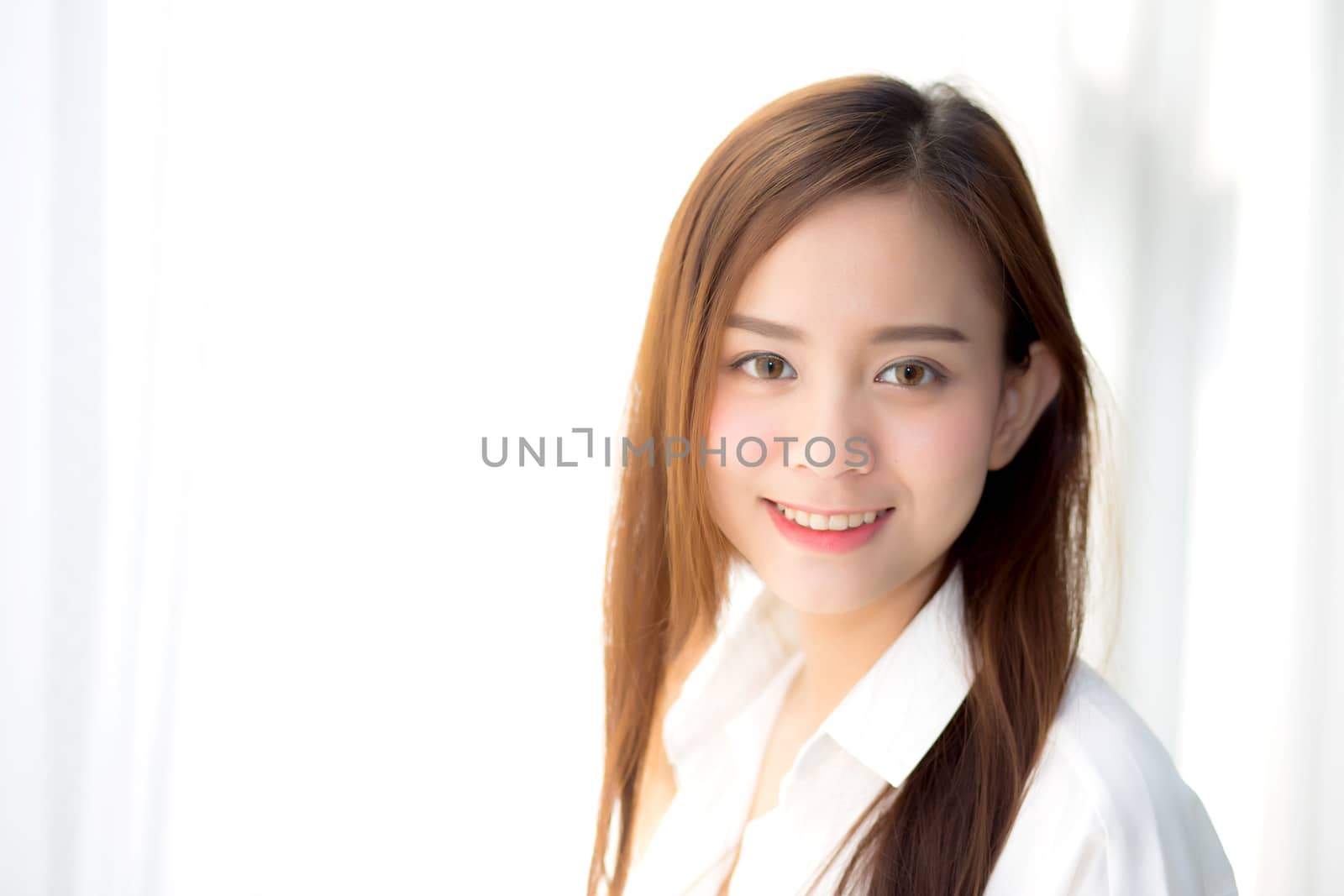 Portrait of beautiful young asian woman standing the window and smile while wake up with sunrise at morning, lifestyle and relax concept.