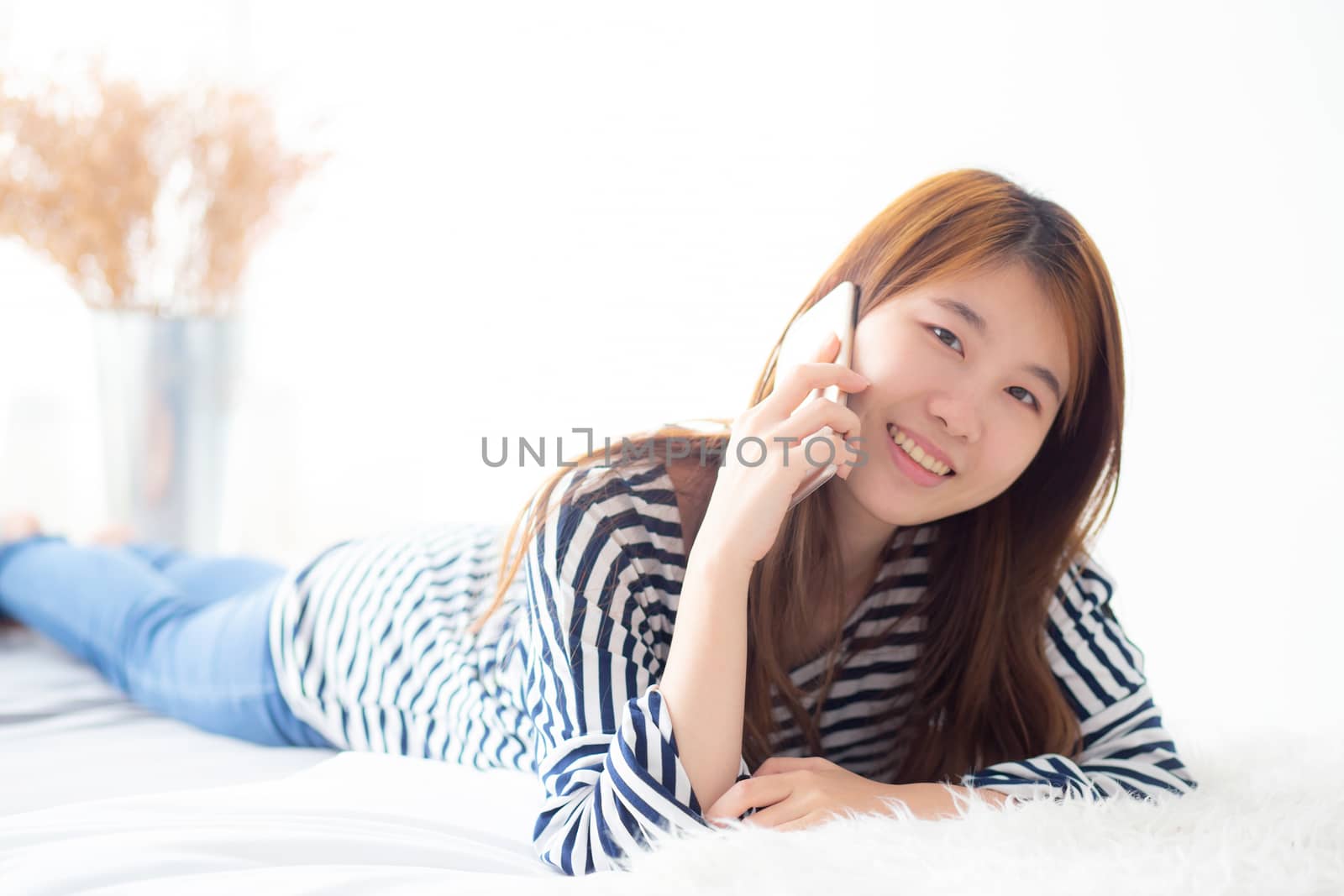 Beautiful young asian woman smiling lying relax on the bed in the morning, girl using mobile smart phone talking enjoy, communication and social network concept.