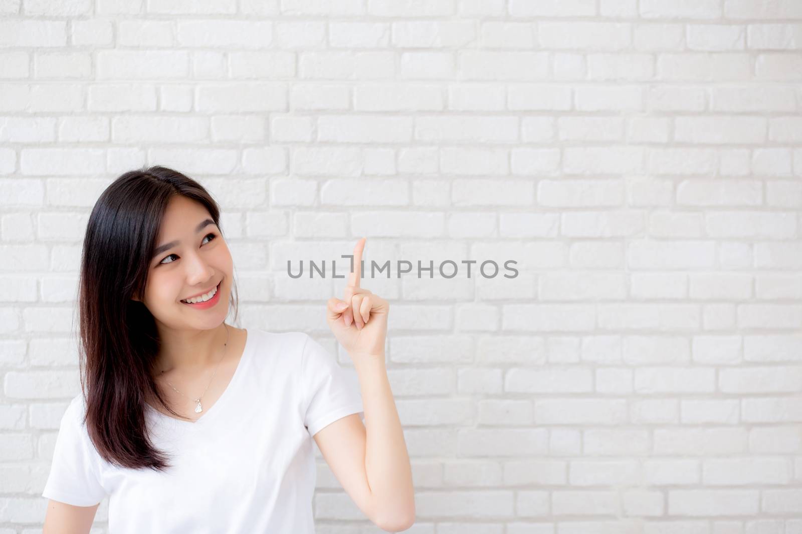 Portrait of beautiful young asian woman happiness standing finger pointing something on gray cement texture grunge wall brick background, businesswoman is a smiling on concrete, business people concept.