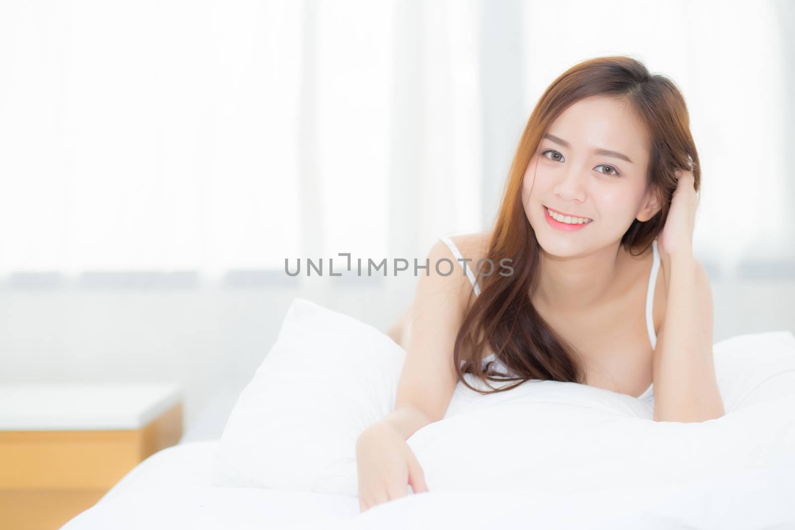 Beautiful portrait young asian woman lying and smile while wake up with sunrise at morning, lifestyle and relax concept.