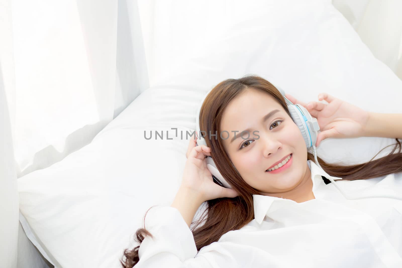 Beautiful asian young woman enjoy listen music with headphone while lying in bedroom, relax girl with earphone internet online, leisure and technology concept.