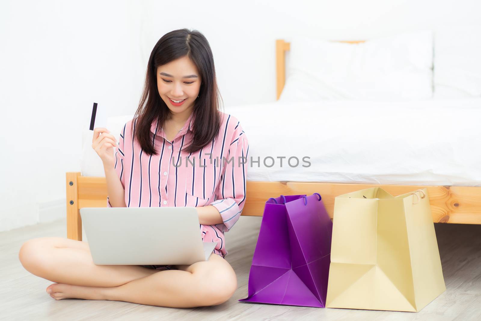 Beautiful of asian woman shopping online with laptop computer sitting on floor on room, girl holding credit card purchase and shopping bags, lifestyle concept.