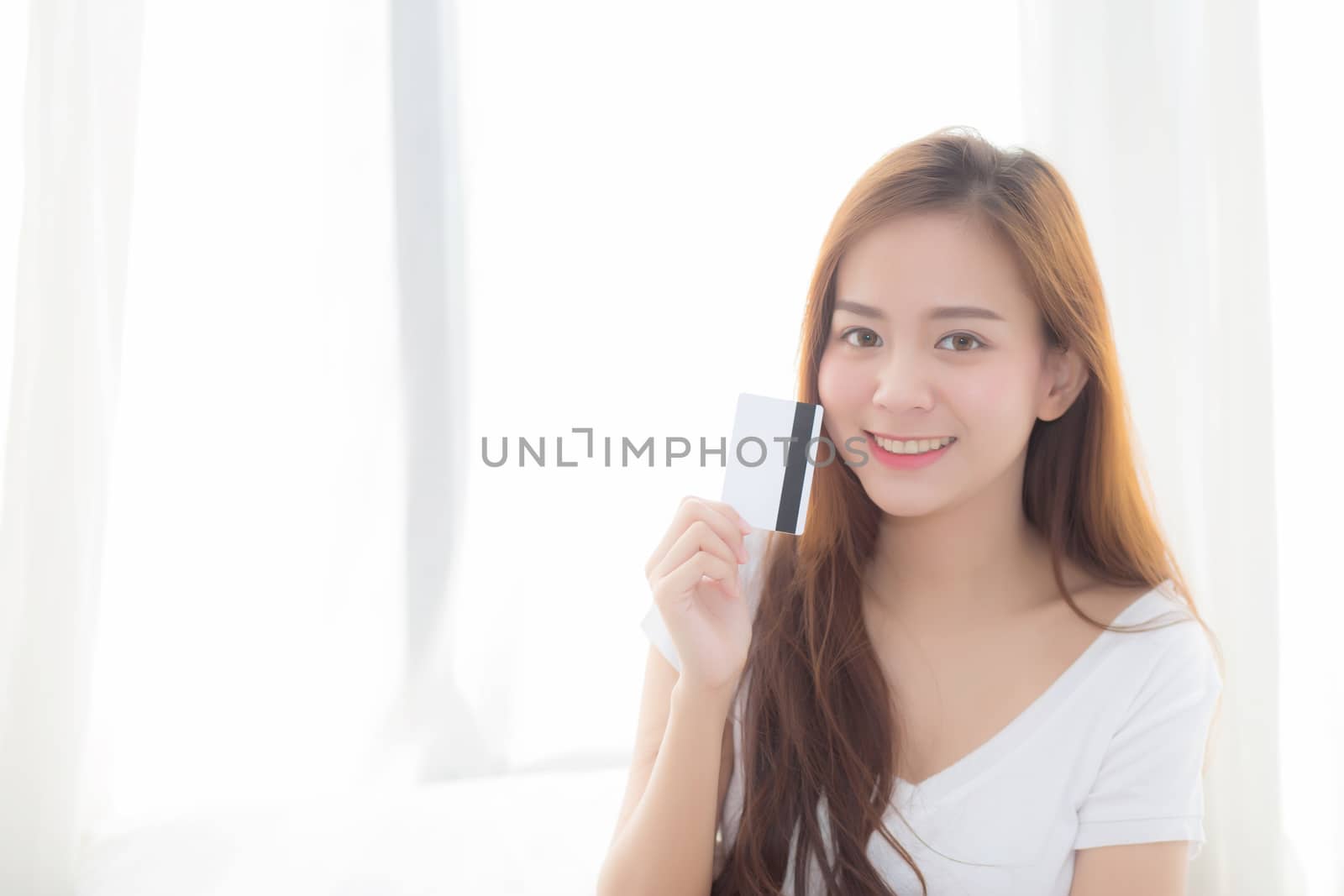 Beautiful asian woman purchase shopping online holding credit card sitting on bed in the bedroom, girl buying to internet, lifestyle concept.