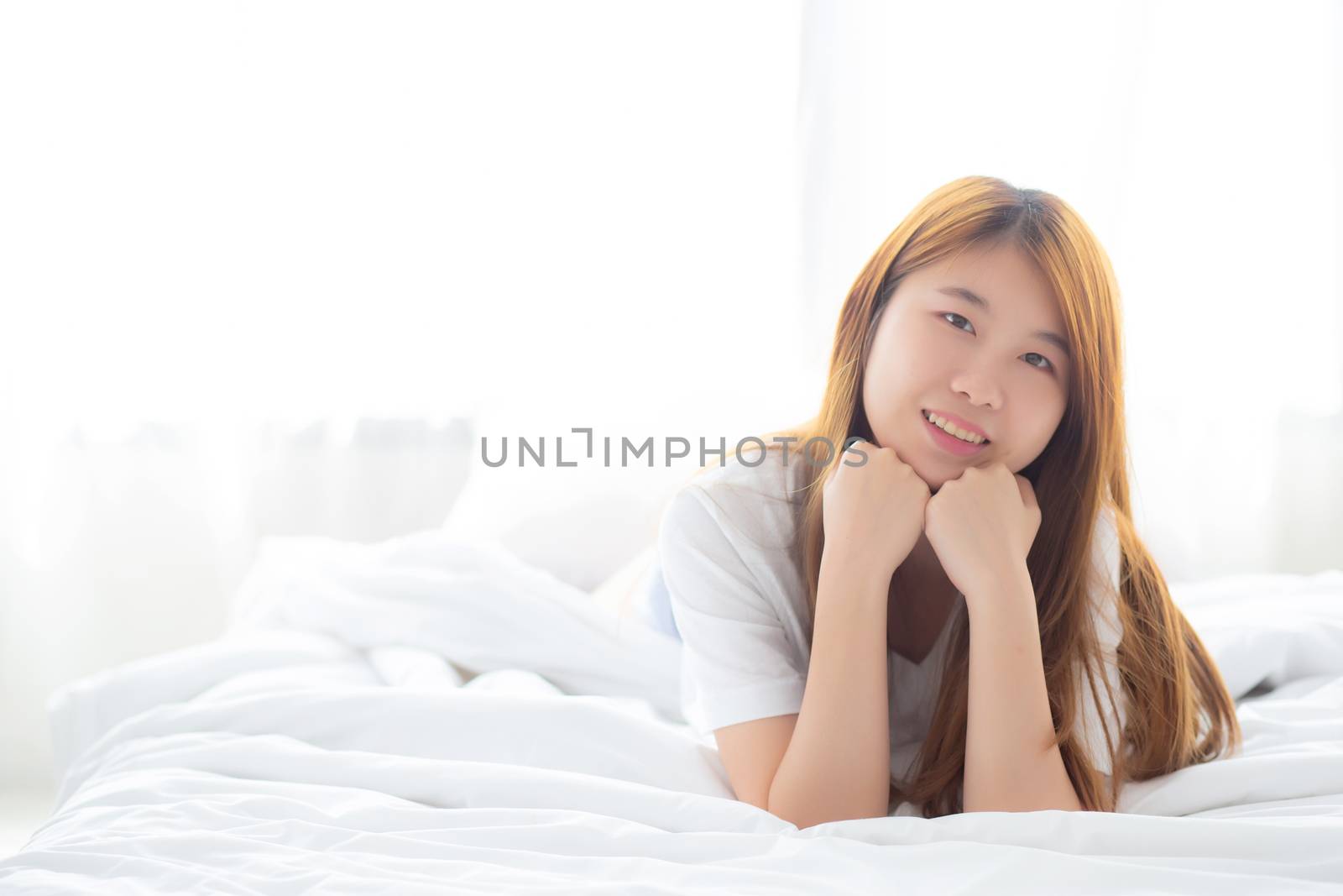 Beautiful portrait young asian woman lying and smile while wake up with sunrise at morning, lifestyle and relax concept.