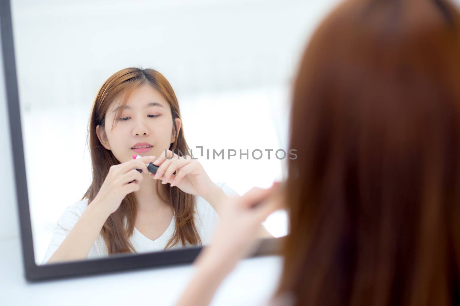 Beauty of portrait of young asian woman at the mirror holding and looking a makeup lipstick, Beautiful girl beauty fashion at the room, lifestyle concept.