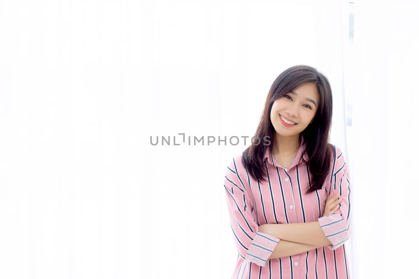 Portrait of beautiful young asian woman standing the window and smile while wake up with sunrise at morning, lifestyle and relax concept.