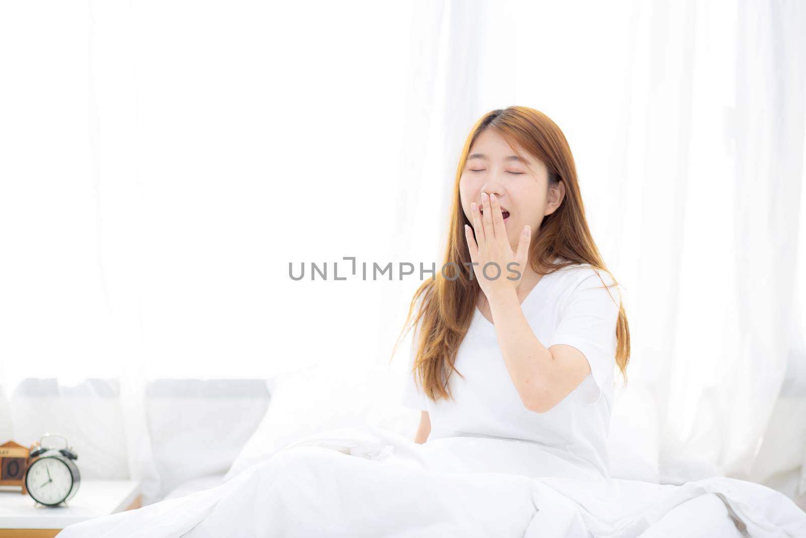Beautiful of portrait young asian woman yawn sitting with sleep on bed at bedroom, girl wake up after resting and leisure with wellness, lifestyle concept.