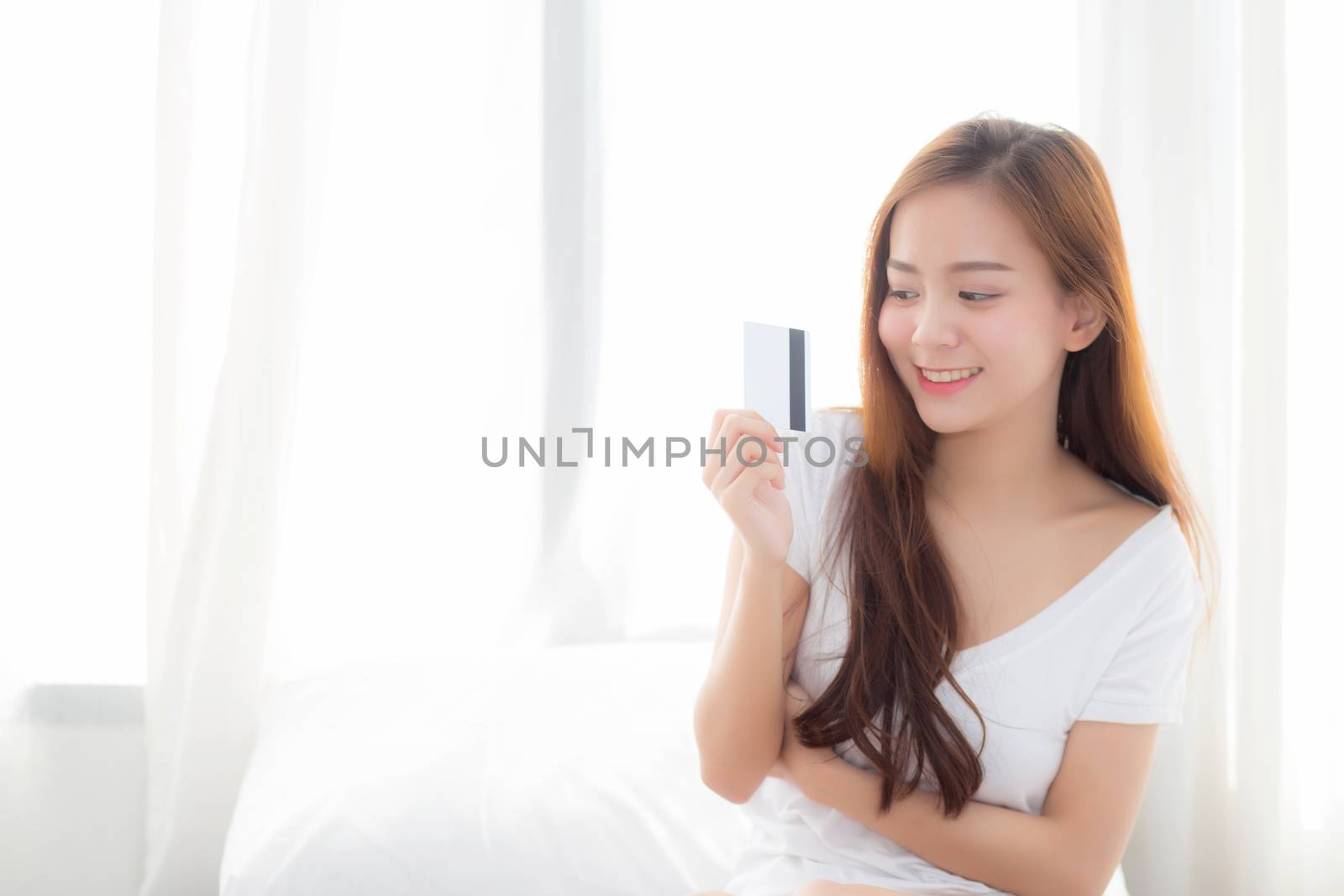 Beautiful portrait young asian woman shopping online with credit card sitting in bedroom, girl with customer purchase of payment online, lifestyle concept.