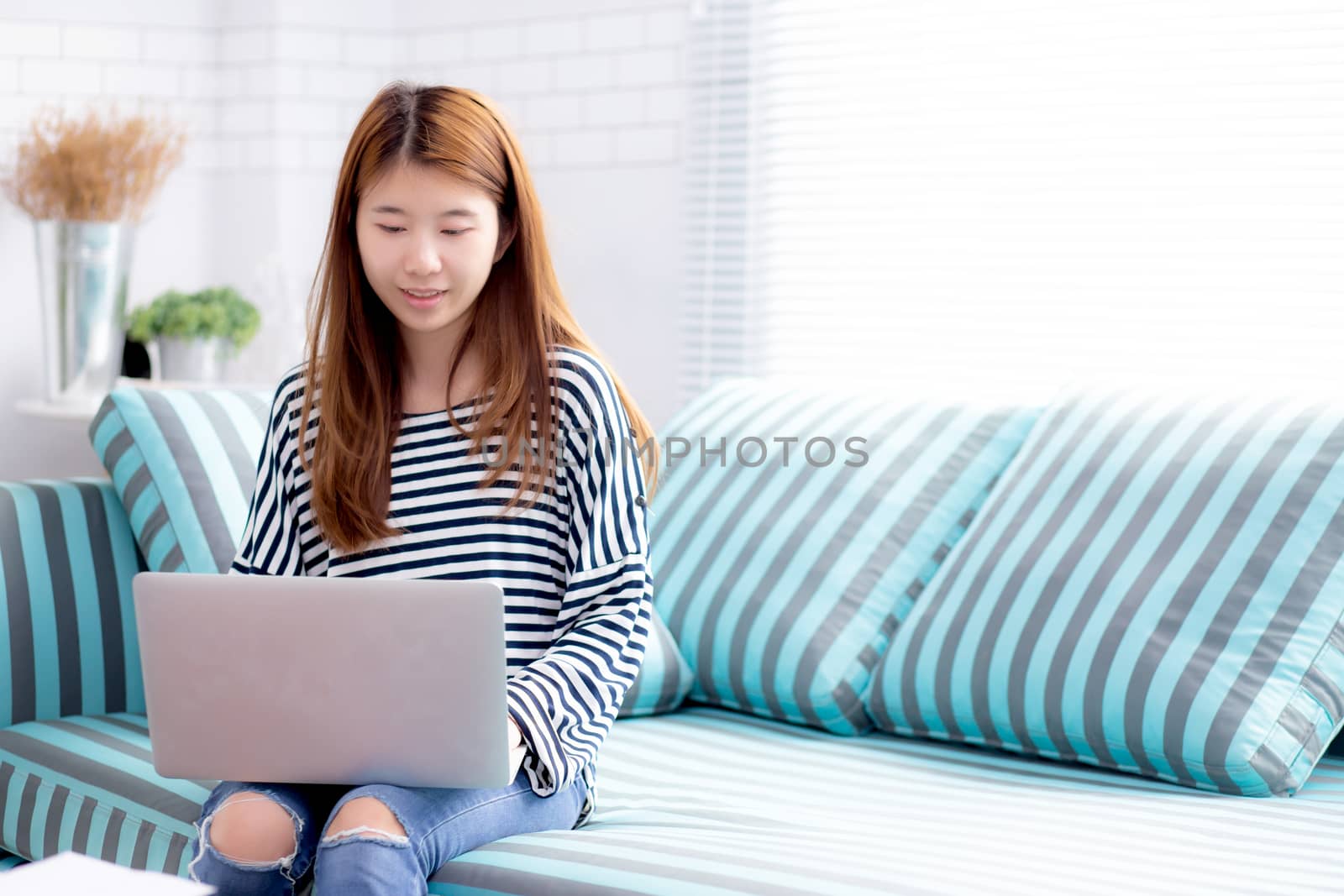 Beautiful of portrait young asian woman using laptop for leisure on sofa in living room, girl working online with notebook freelance with a happy, communication business concept.