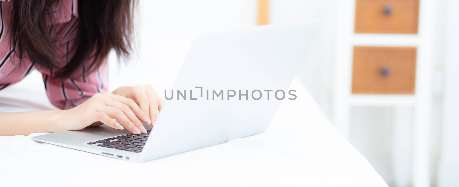 Closeup banner website asian young woman lying on bed using laptop at bedroom for leisure and relax, freelance with girl working notebook, communication concept.