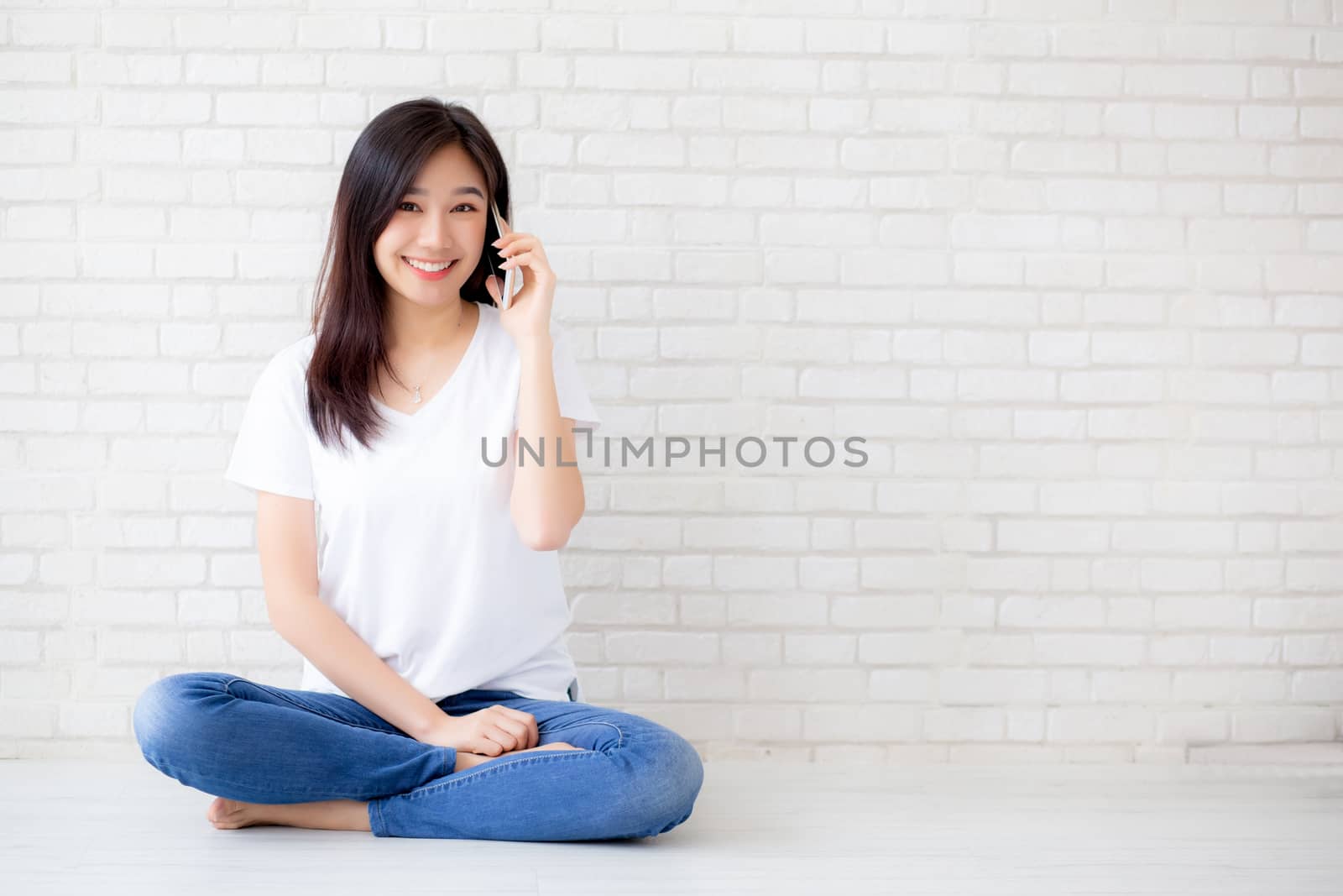 Beautiful of portrait young asian woman talk smart phone and smile sitting on cement concrete brick background, freelance female calling telephone, communication of mobile concept.