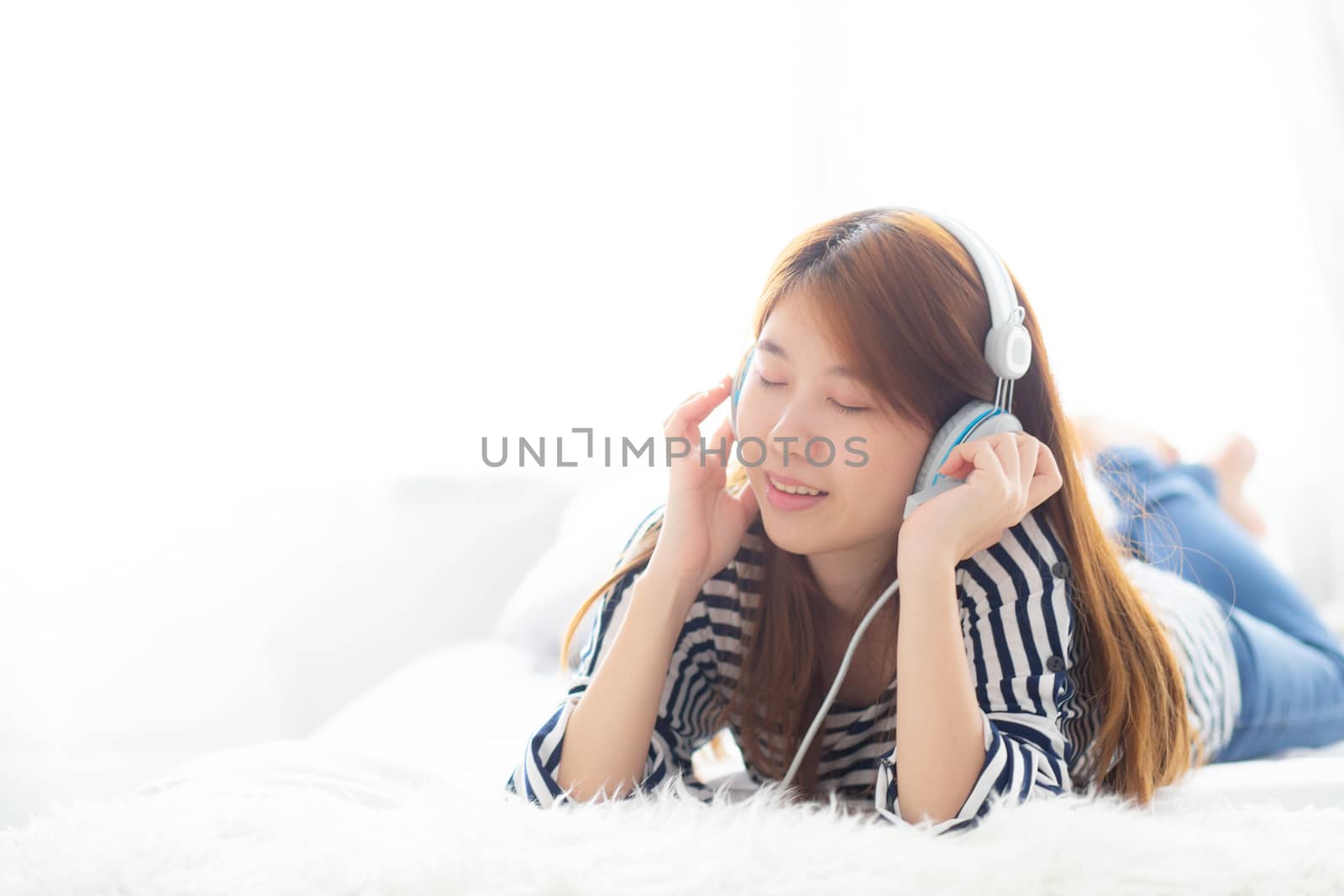 Beautiful asian young woman enjoy and fun listen music with headphone lying in bedroom, girl relax with earphone, leisure and technology concept.