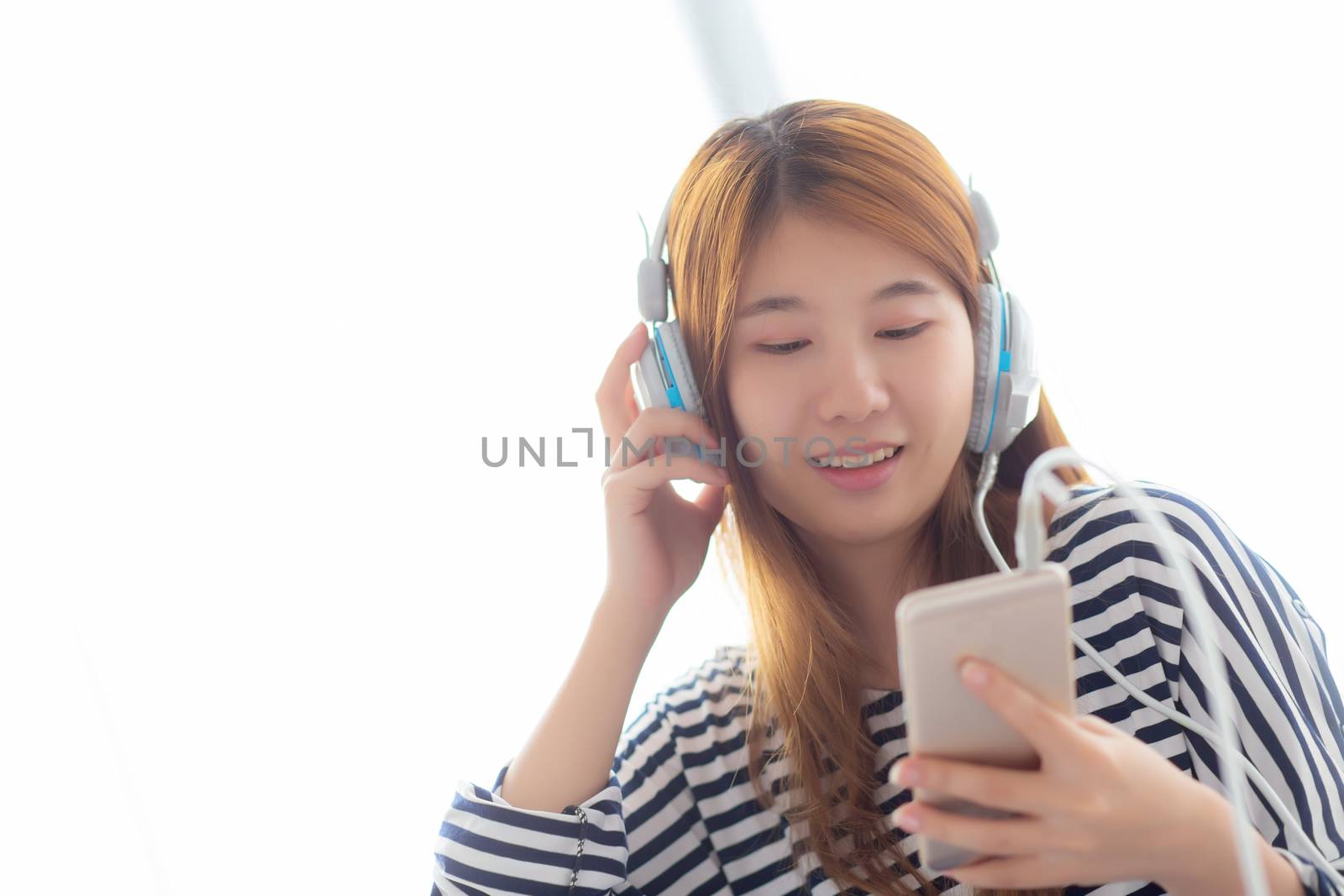 Beautiful asian young woman enjoy listen music with headphone and holding smart mobile phone while sitting in bedroom, relax girl with earphone, leisure and technology concept.