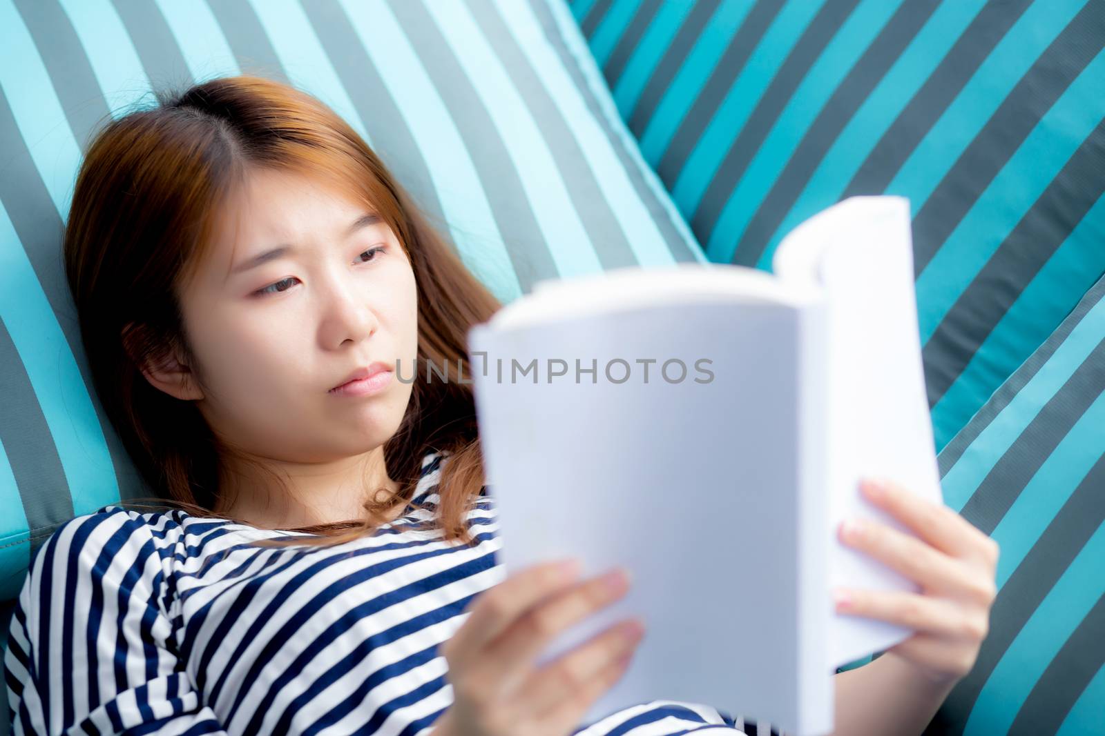 Beautiful of portrait young asian woman relax lying reading book on sofa in bedroom at home, girl study literature, education and lifestyle concept.