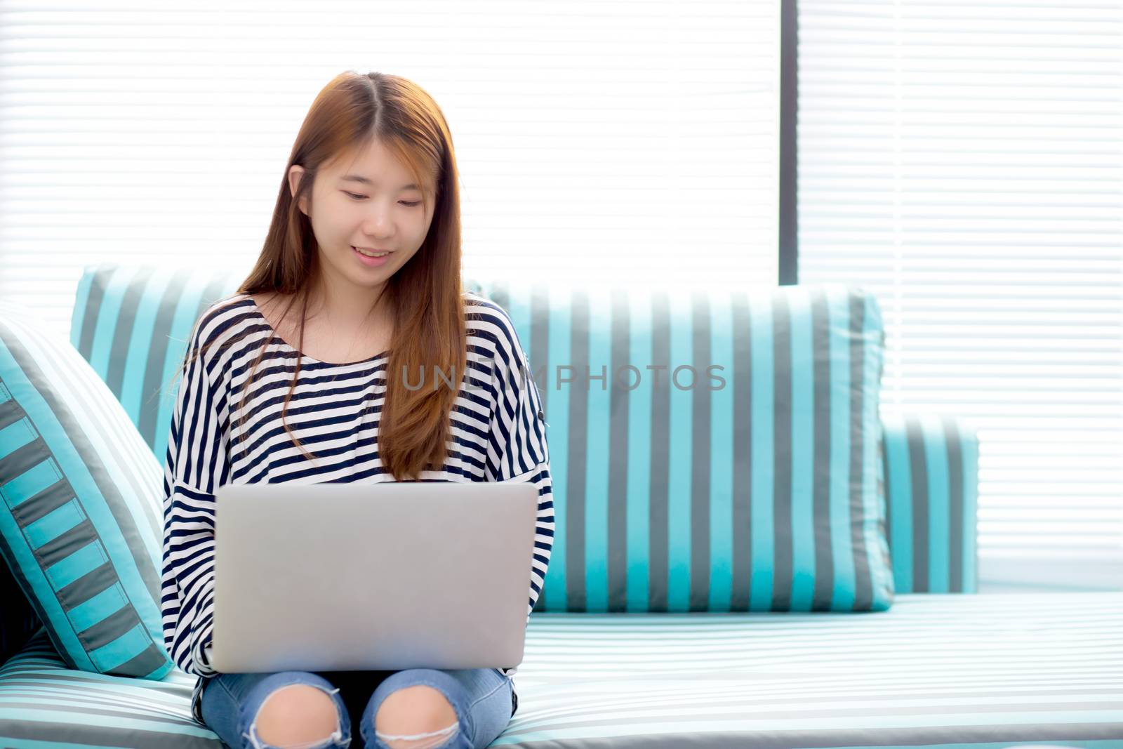Beautiful of portrait asian young woman working online laptop sitting on sofa at living room, girl using notebook computer with connect to internet, business and success concept.