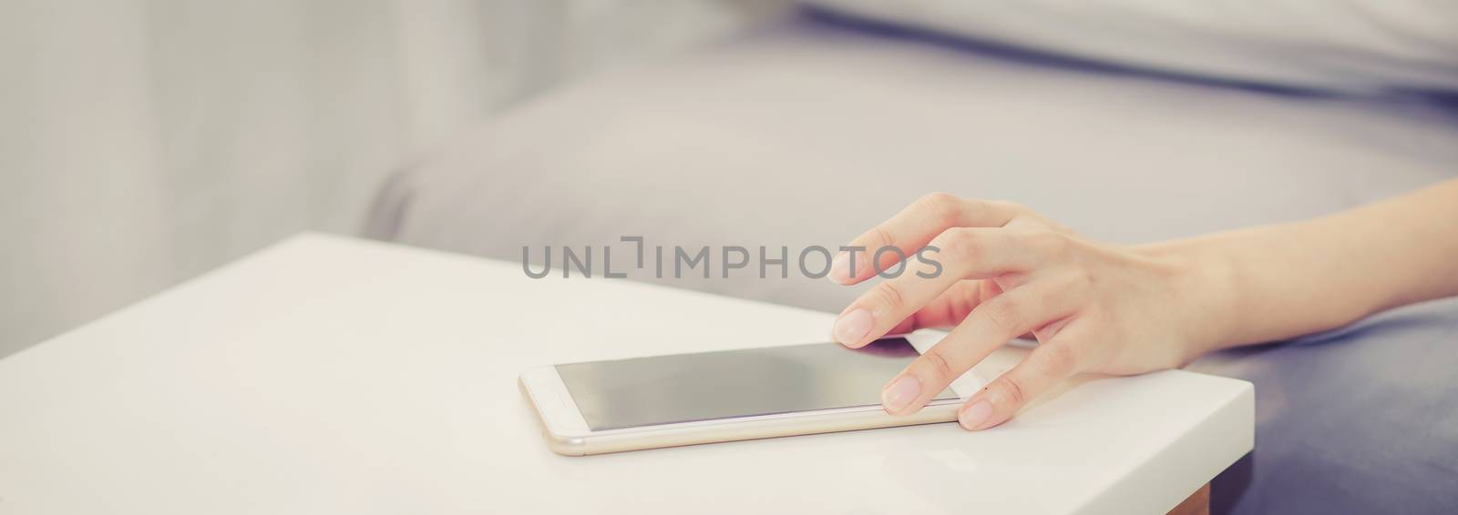 Closeup banner website hand of woman turn off alarm on call mobile phone while wake up after sleep relax in good morning at bedroom, vintage tone.