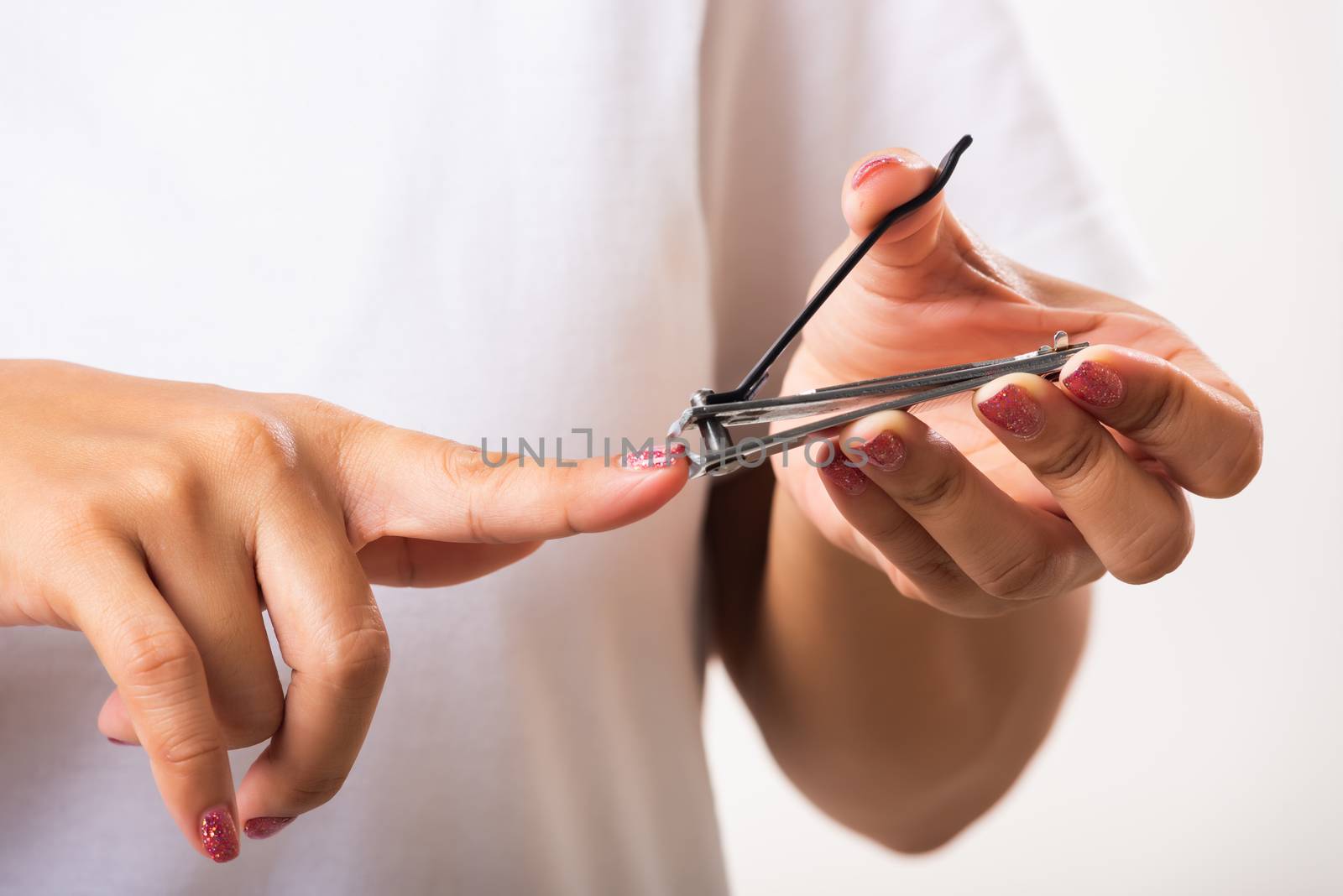 Close up young Asian woman have tool cutting nails fingernails on finger using a nail clipper. Female using tweezers by herself, studio shot isolated on white background, Healthcare concept