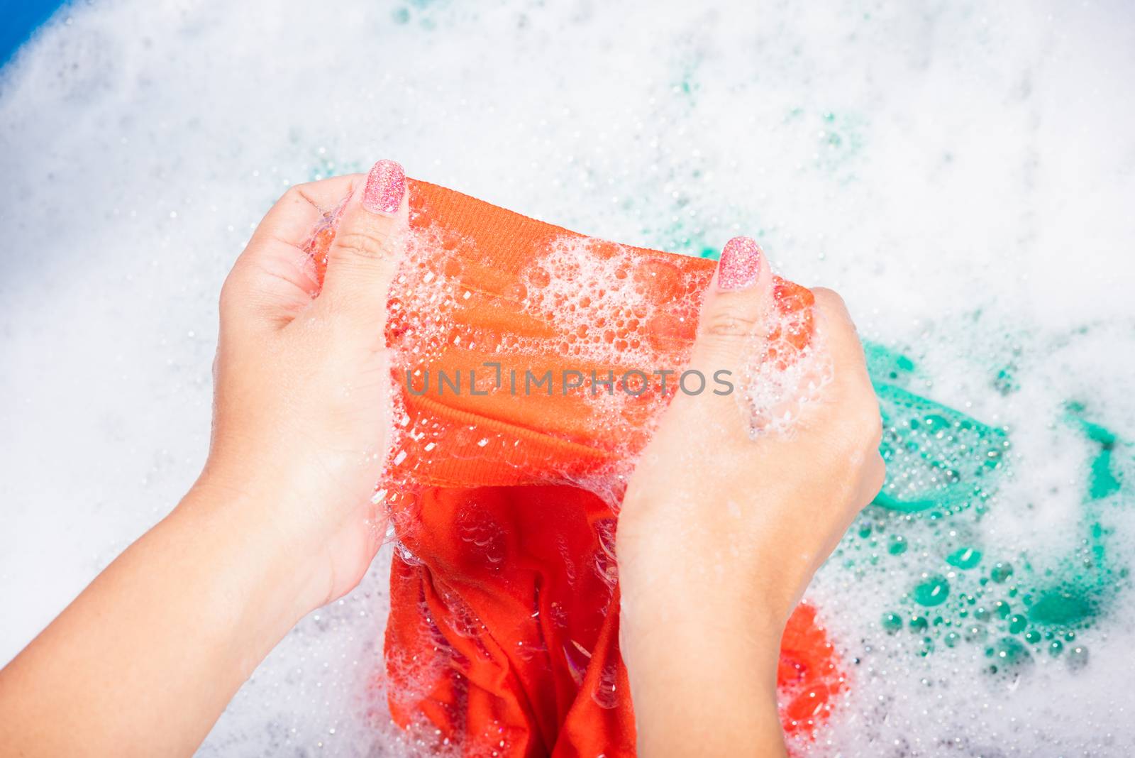 Closeup young Asian woman use hands washing color clothes in basin with detergent have soapy bubble water, studio shot background, laundry concept