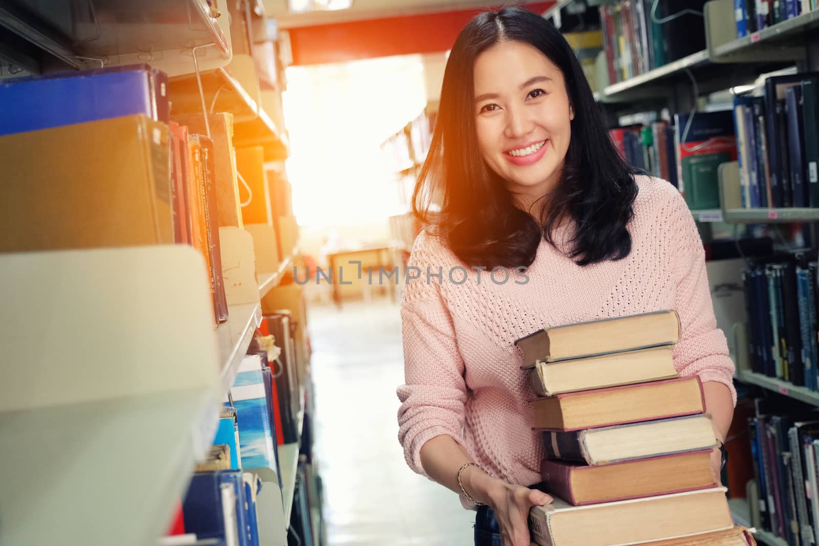 Young woman carrying heavy books in library by Surasak