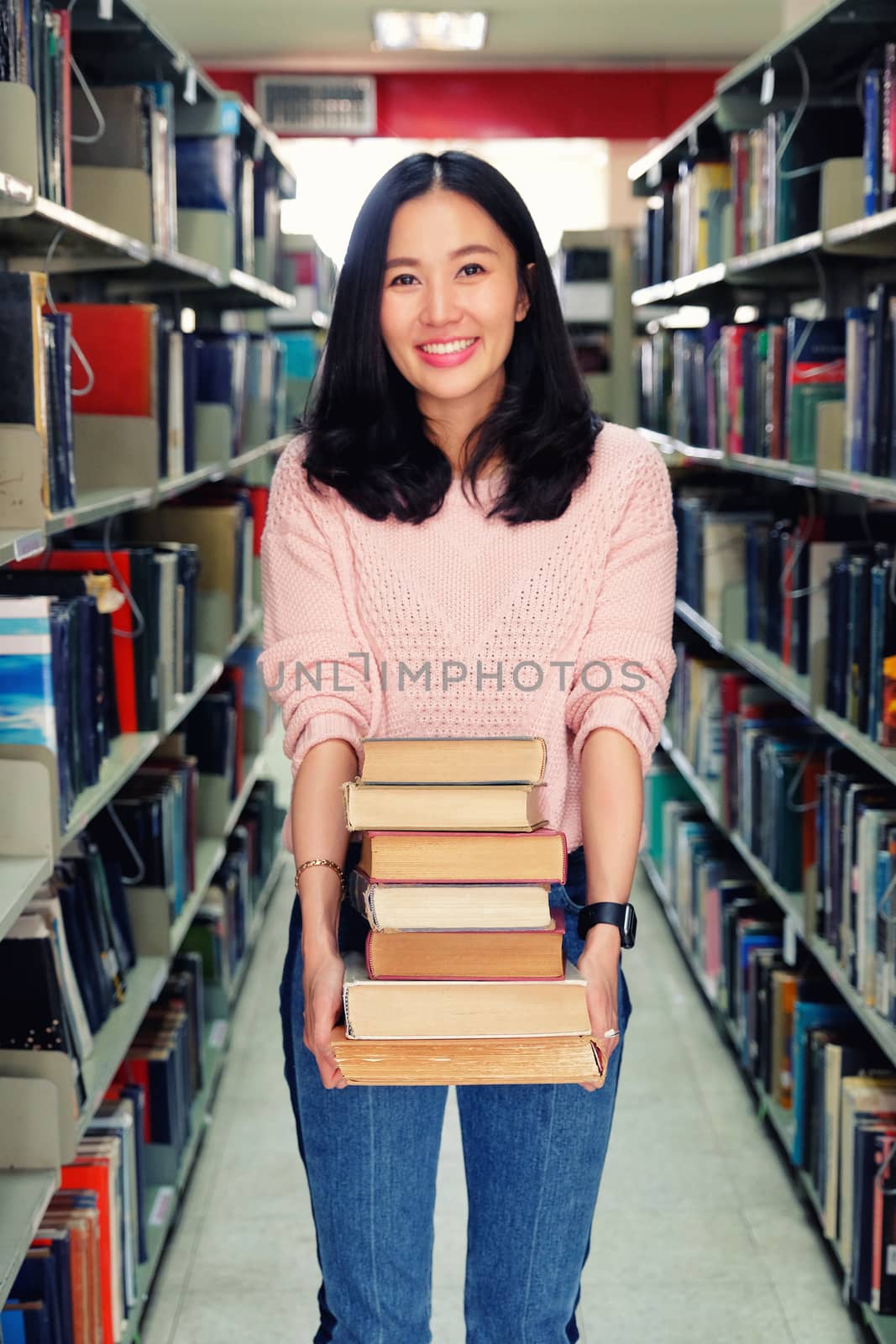 Young woman carrying heavy books in library by Surasak