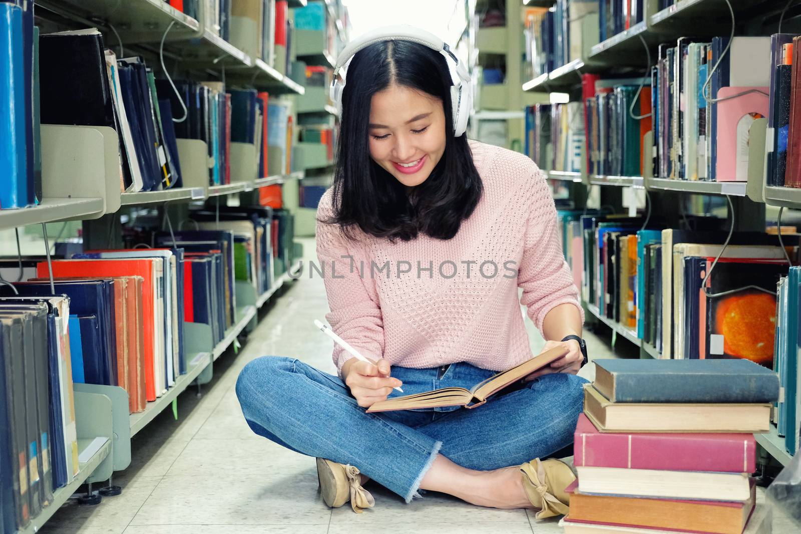 Young woman in a good mood listening to music  while studying in a library