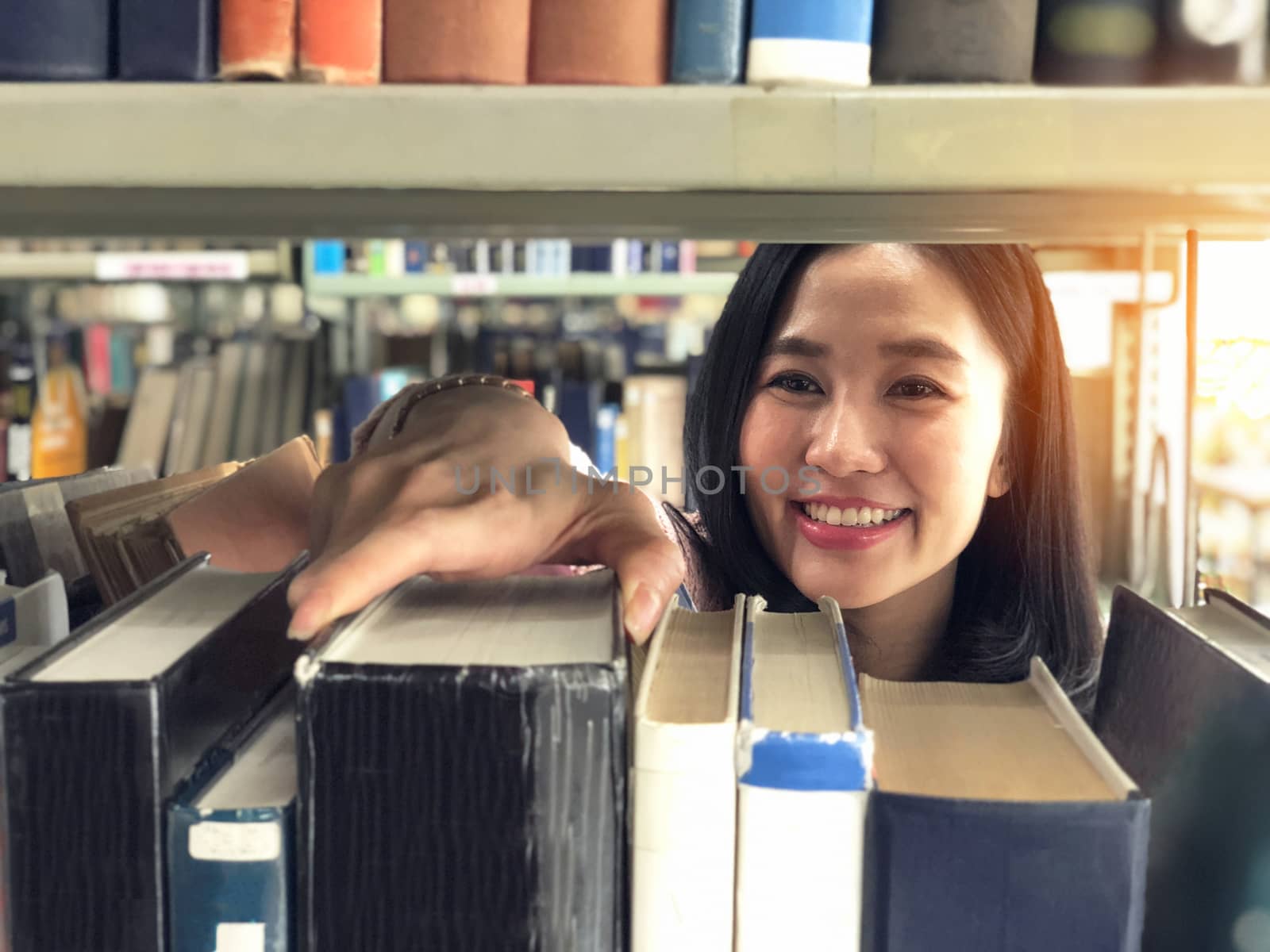 Young woman picking a book off the shelf in a library by Surasak