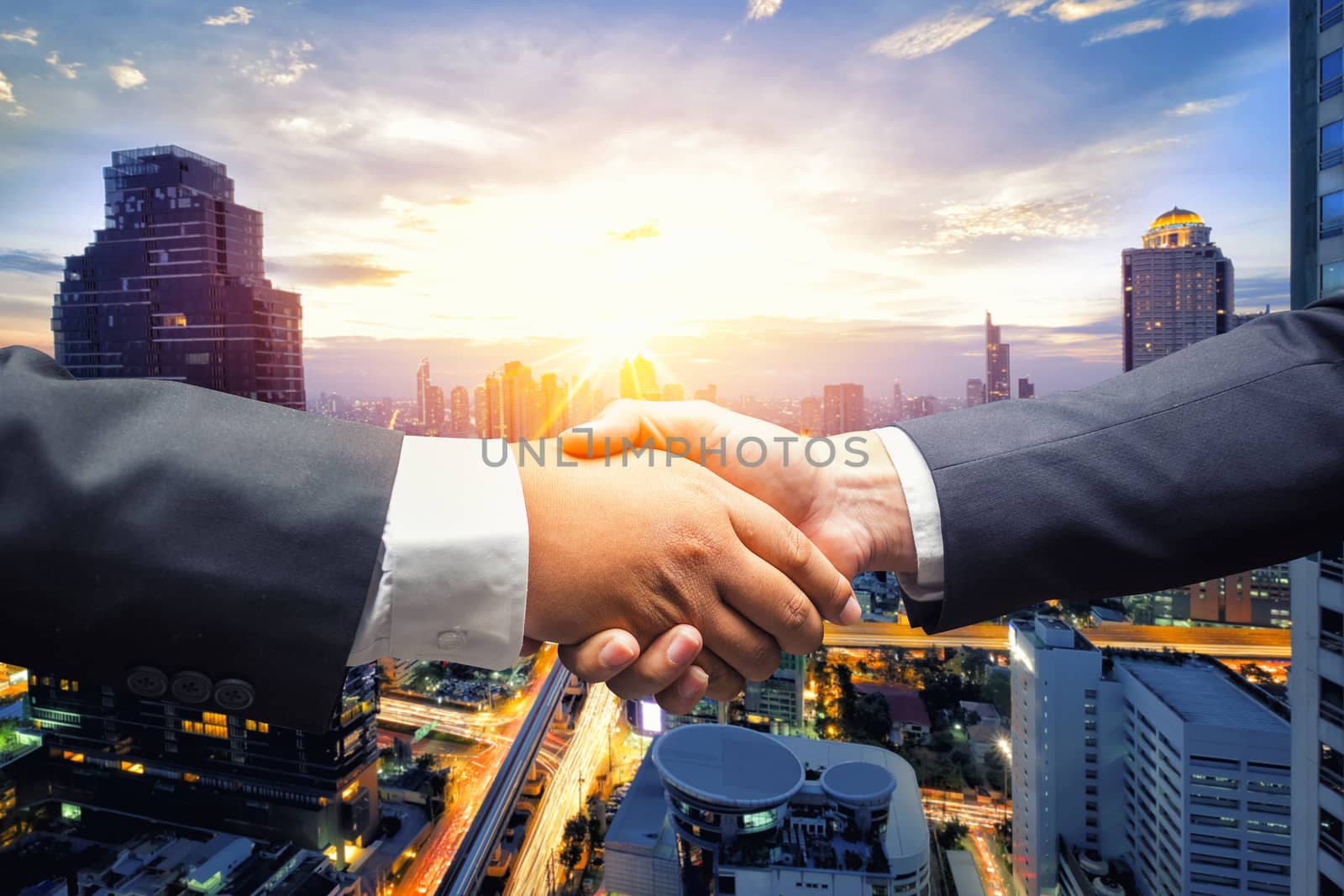 Business men shaking hands on cityscape business background by Surasak
