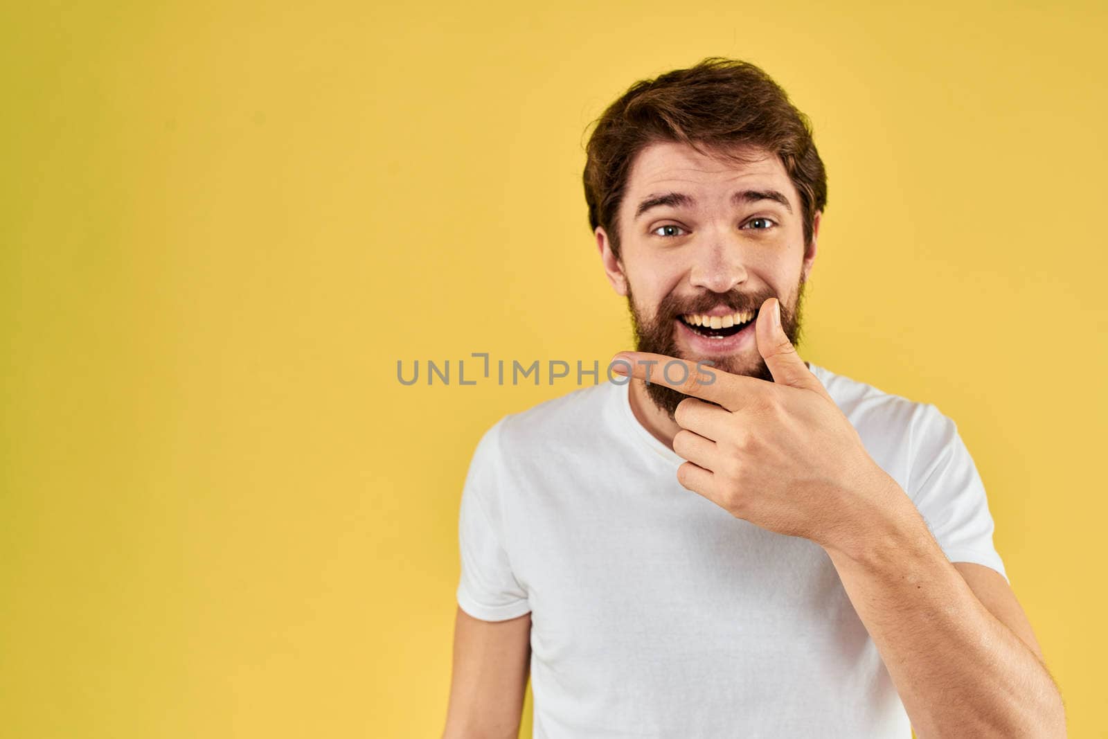 Bearded man emotions fun gesture with hands white t-shirt close-up yellow background. High quality photo